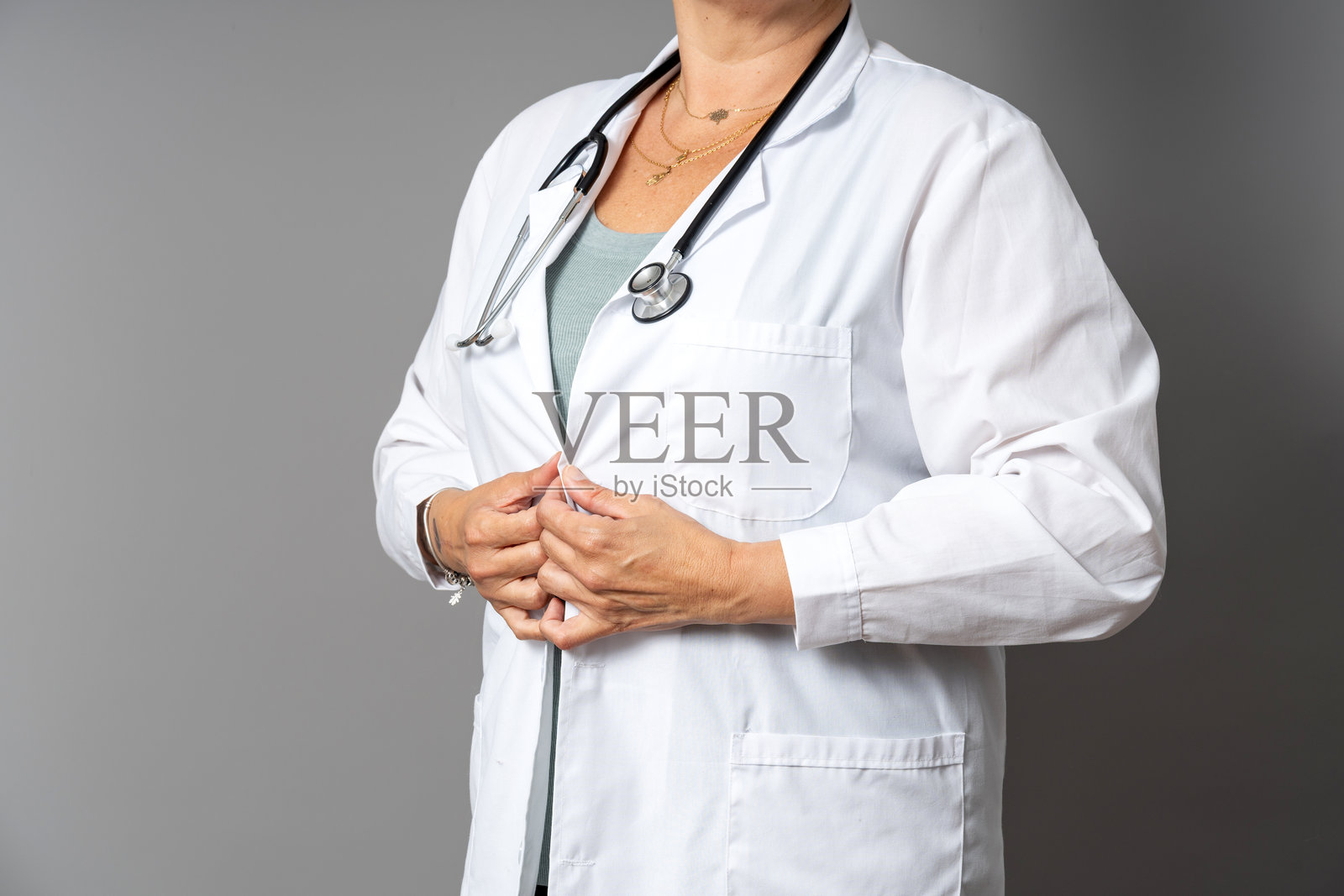 成熟的女性医生在灰色背景下扣上白大褂照片摄影图片