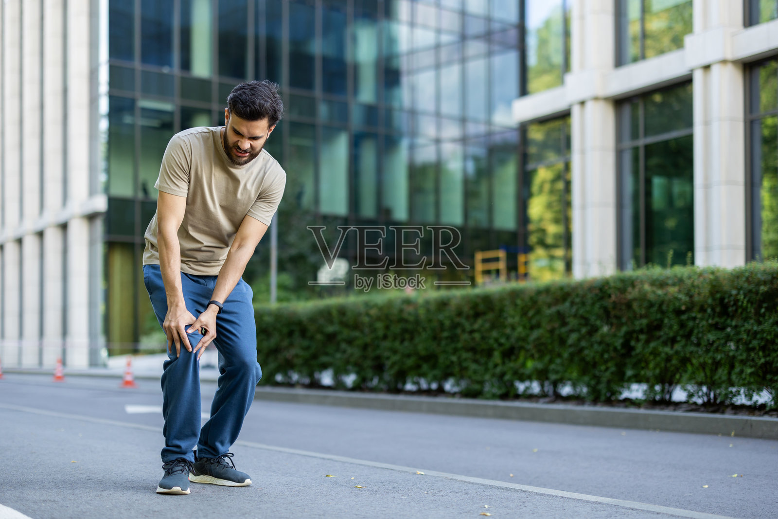 一位印度年轻男子在户外忙于跑步和锻炼，受伤后痛苦地歪着身子，捂着膝盖。照片摄影图片