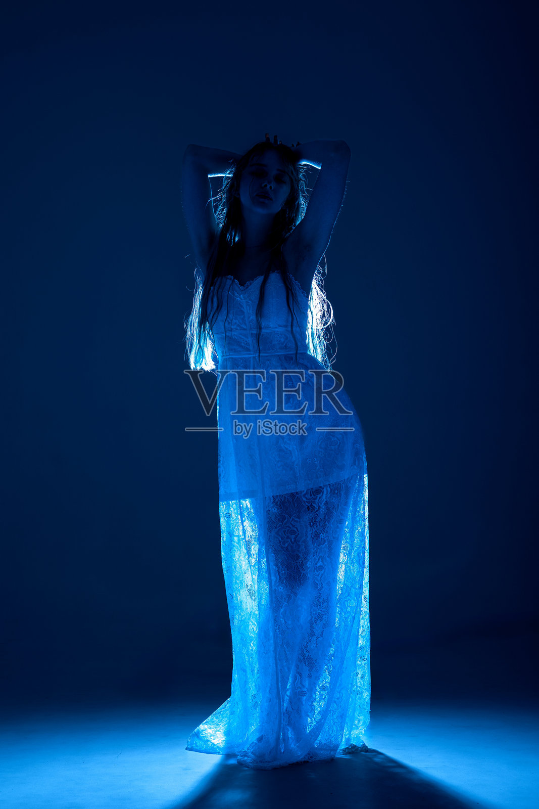 优雅的女性剪影，身穿飘逸的白色裙子，在黑暗的工作室空间中被蓝光照亮照片摄影图片