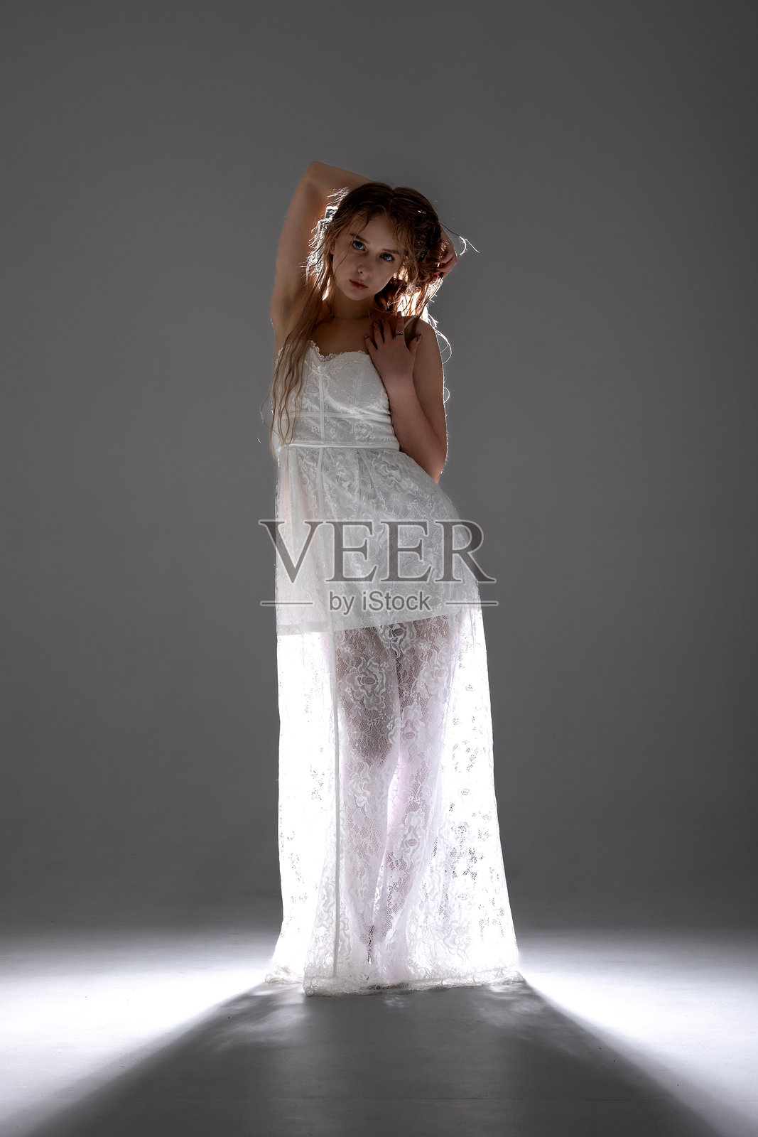 模特在夜间的摄影棚中自信地穿着优雅的白色裙子，灯光效果极具戏剧性。照片摄影图片