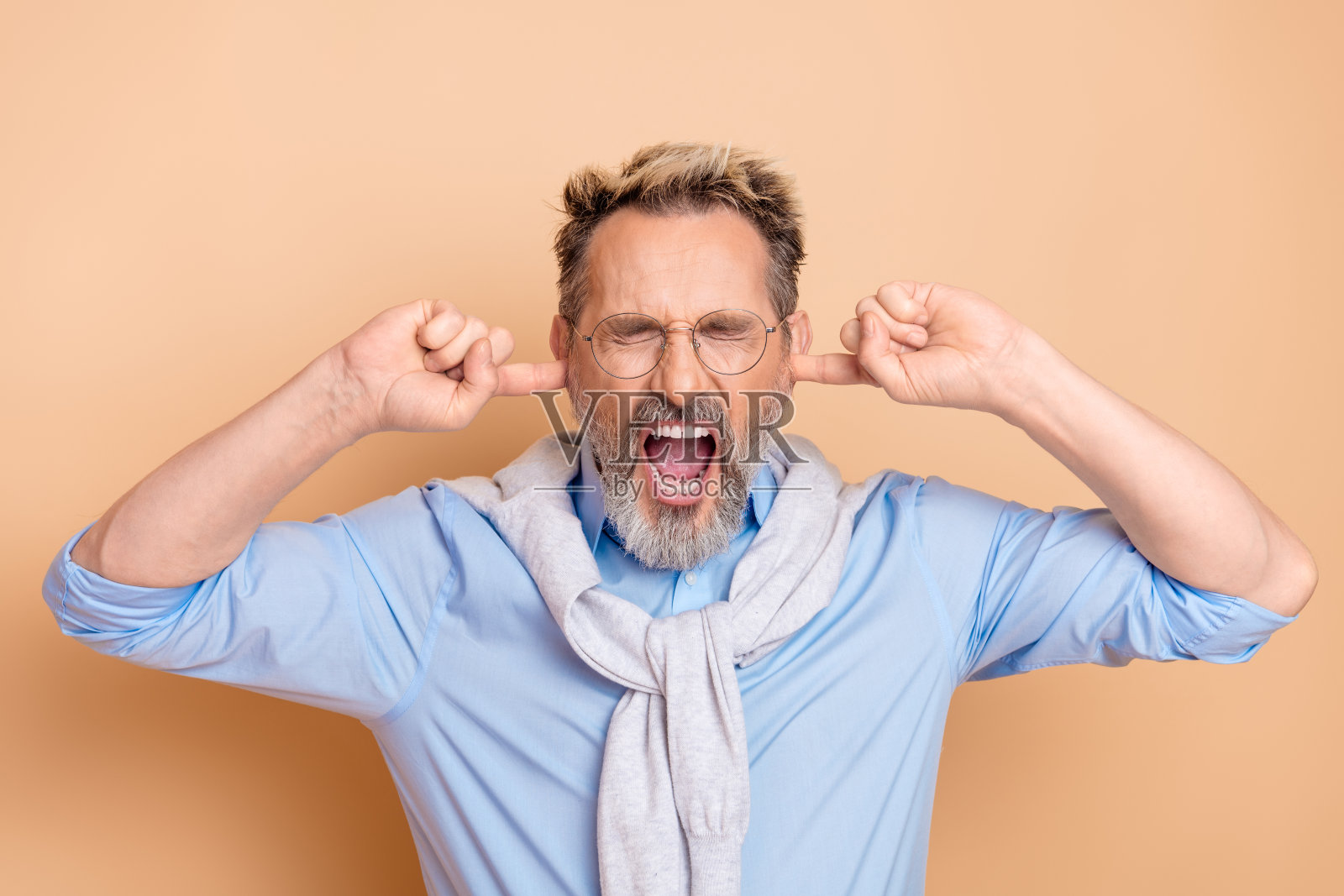 成熟的商人因沮丧而捂住耳朵，面部表情丰富，背景为米色。照片摄影图片