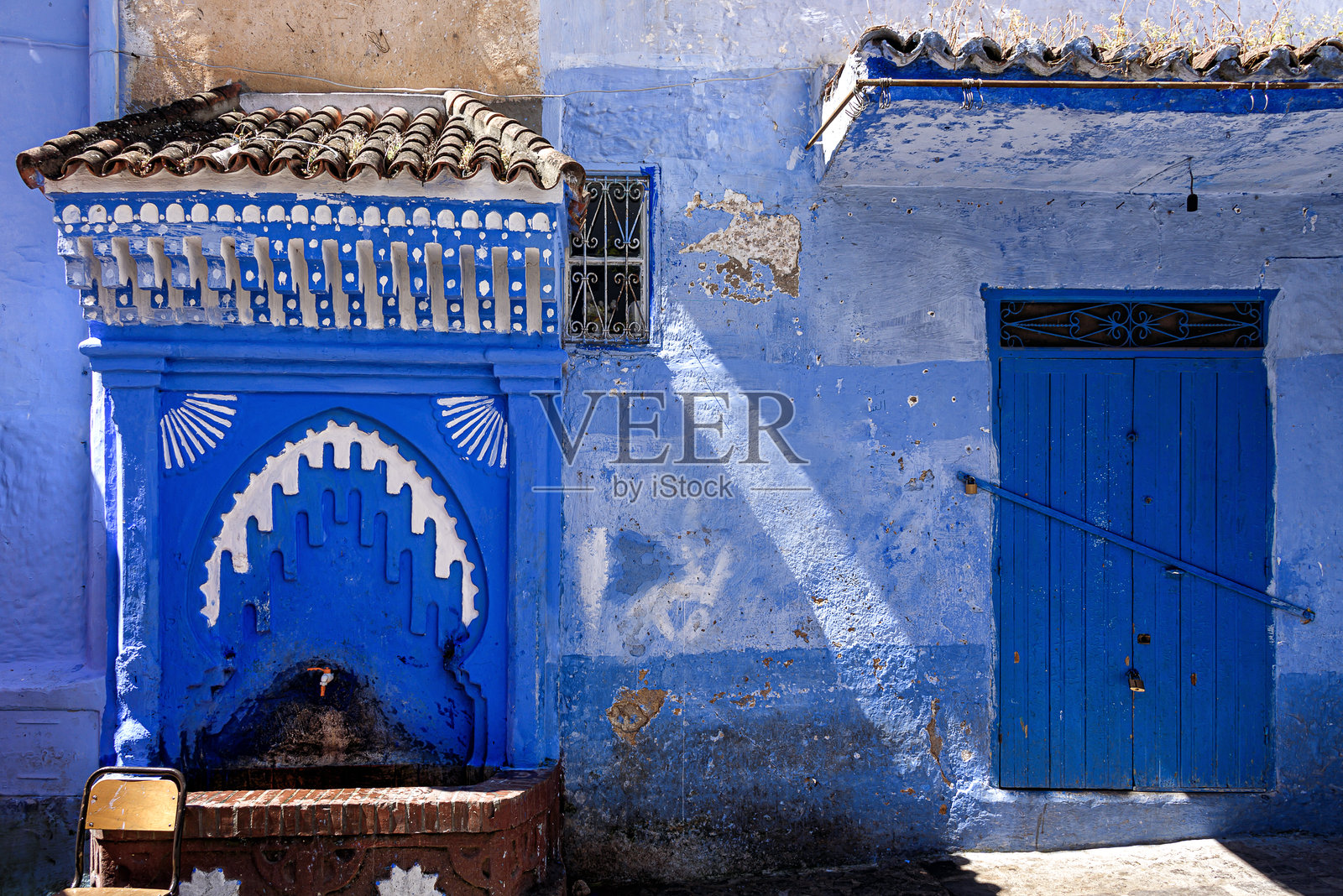 摩洛哥舍夫沙万美丽的蓝色麦地那中，一座精美雕刻的户外喷泉和一扇蓝色木门。照片摄影图片