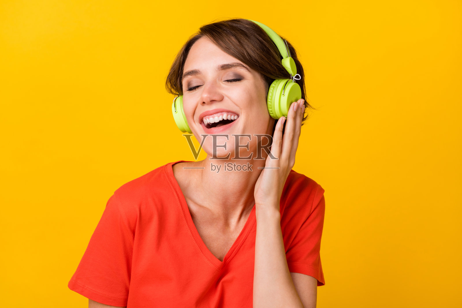 可爱的无忧无虑的人闭着眼睛，手臂触碰耳机，背景为黄色。照片摄影图片