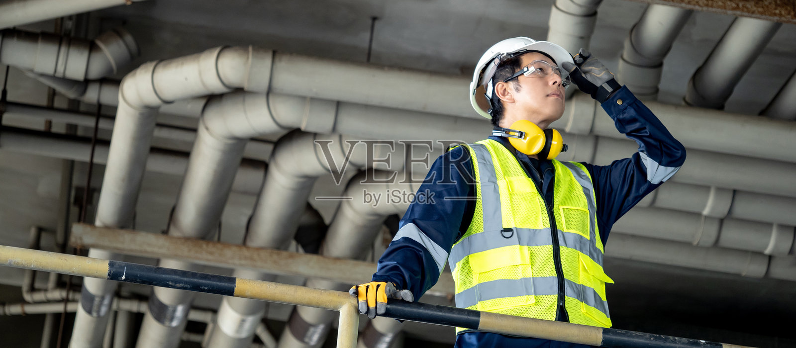 亚洲男性检验工程师手持安全头盔，正在查看建筑工地的管道系统。照片摄影图片