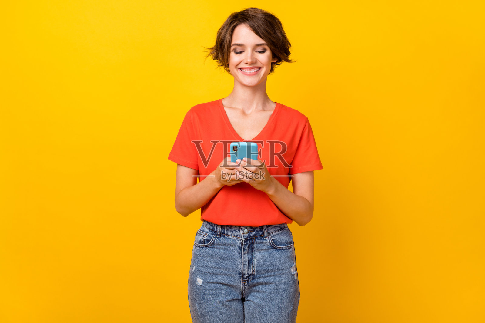 迷人快乐的女士微笑着，手持手机打字评论，背景为黄色。照片摄影图片