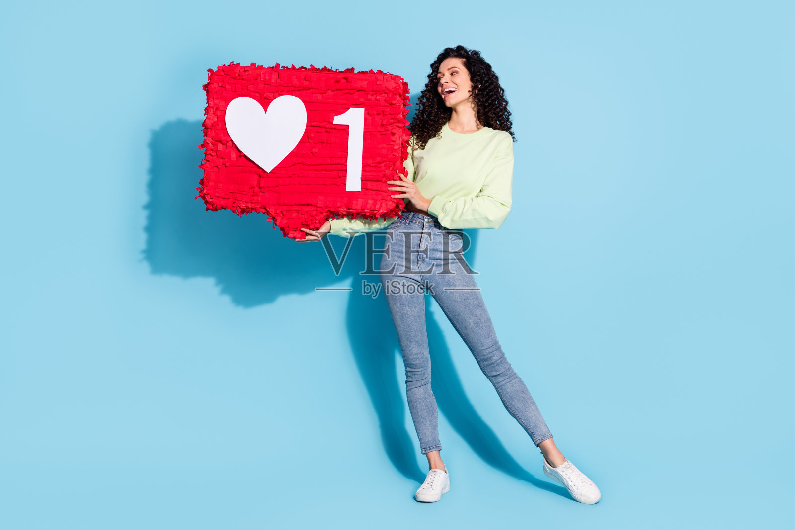 迷人的全身肖像，双臂抱着像纸拼贴一样的大物体，背景为蓝色。照片摄影图片