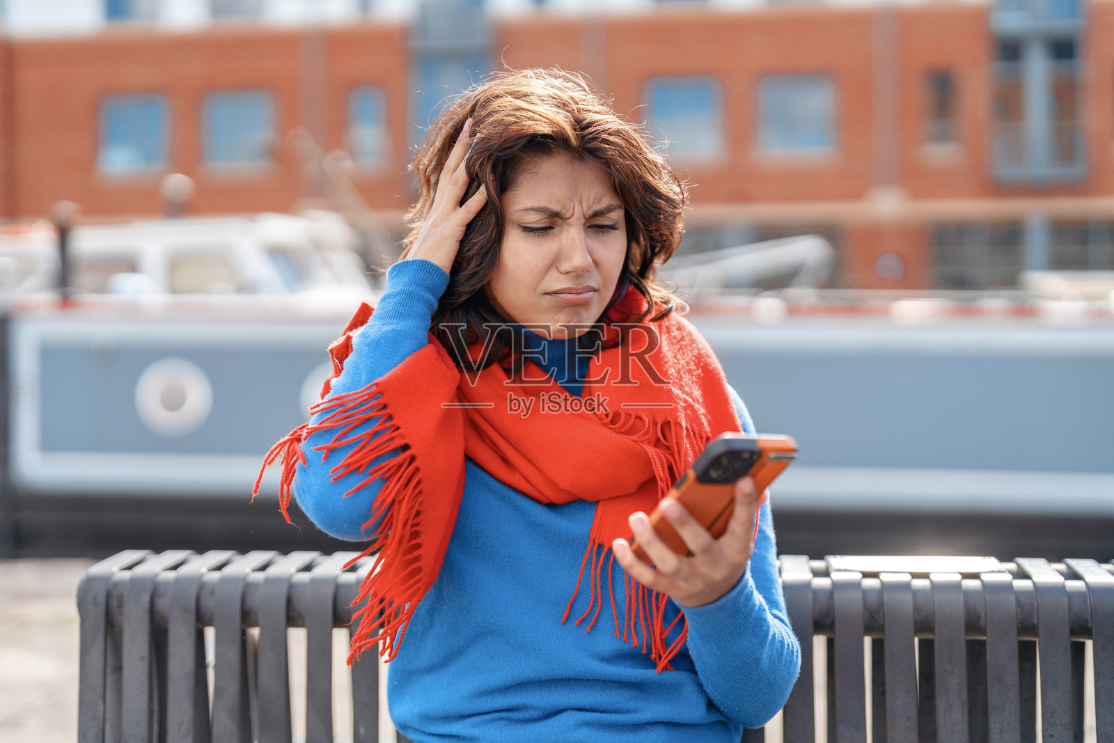 沮丧的女人在阳光明媚的日子里坐在码头旁的长椅上查看手机照片摄影图片