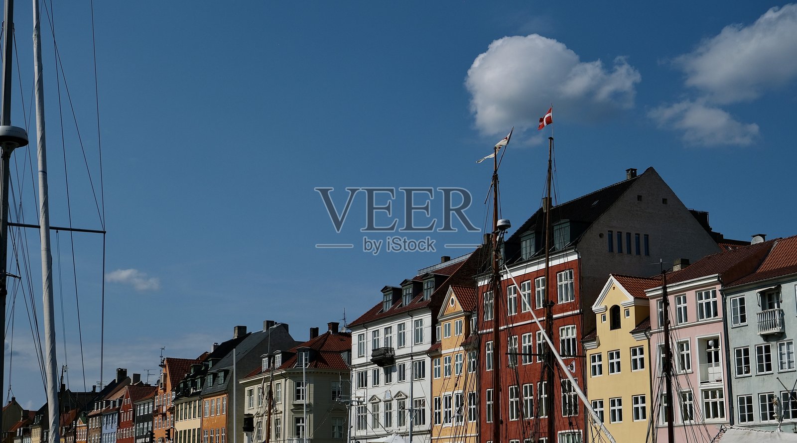 哥本哈根尼哈芬的五彩斑斓的海滨房屋和船只，晴朗的夏空和孤立的蓬松云朵。照片摄影图片