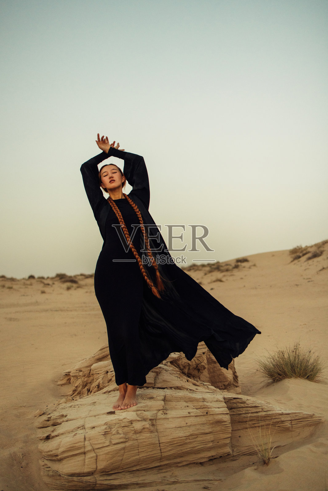 优雅的女性身着黑色长裙，在宁静的沙漠环境中摆姿势照片摄影图片