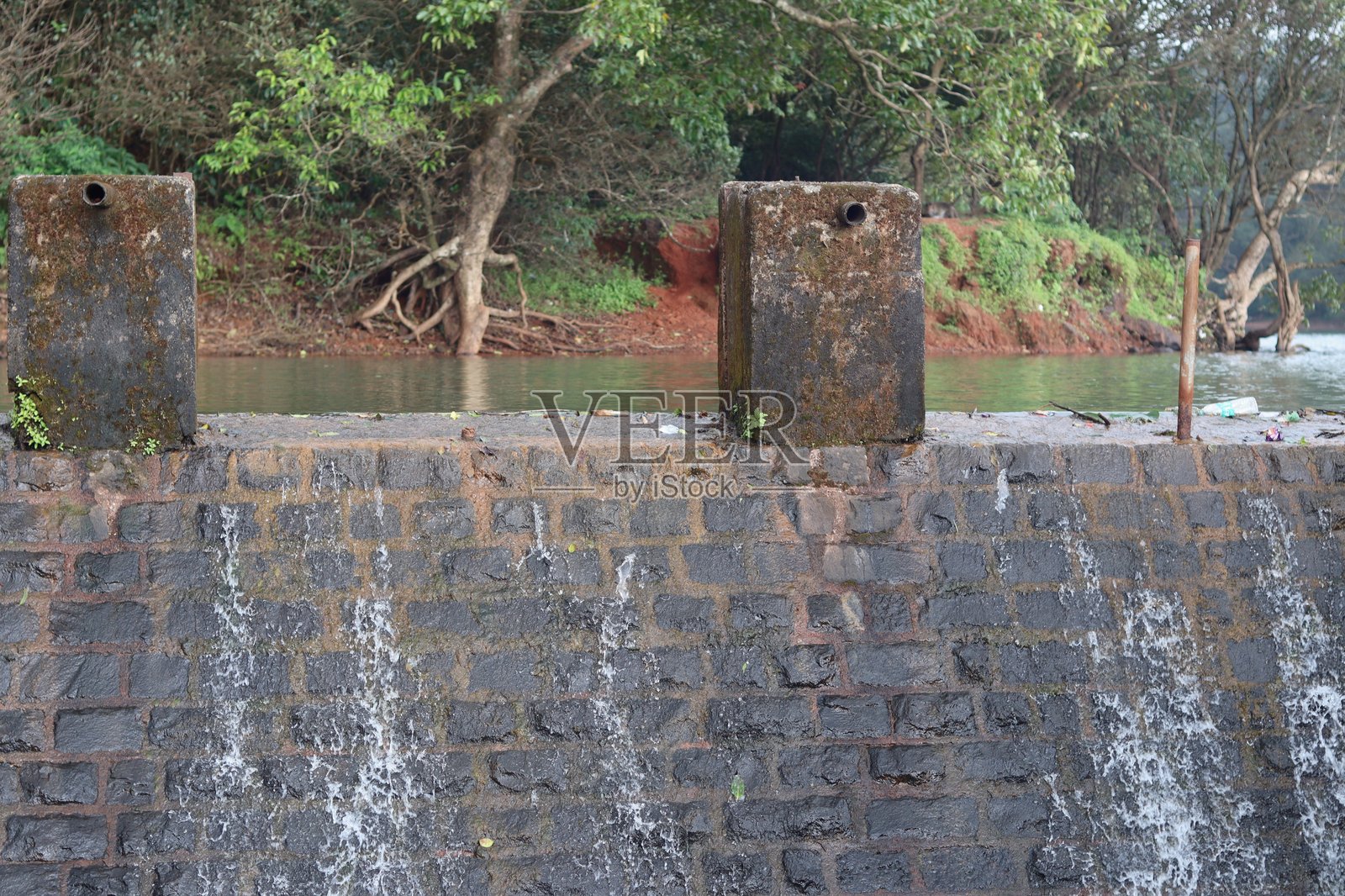 一小股水流从马瑟兰的石坝墙上缓缓流过，四周被森林环绕。照片摄影图片