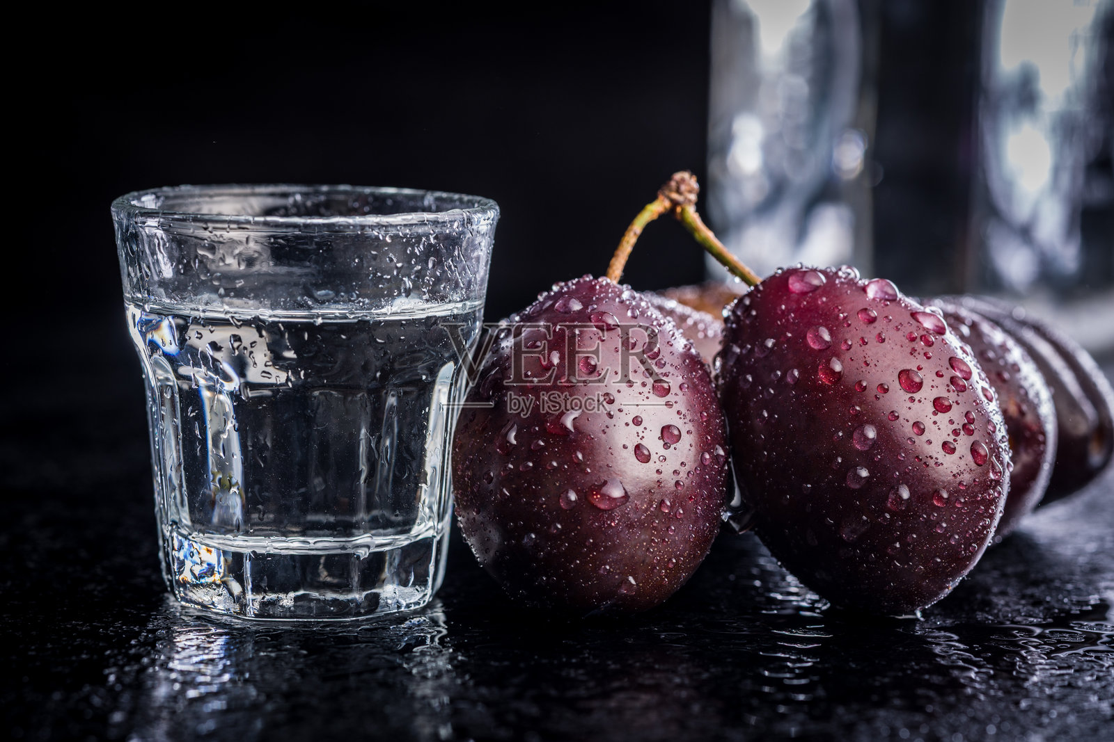 黑色桌子上的李子和蒸馏酒。李子白兰地酒。照片摄影图片