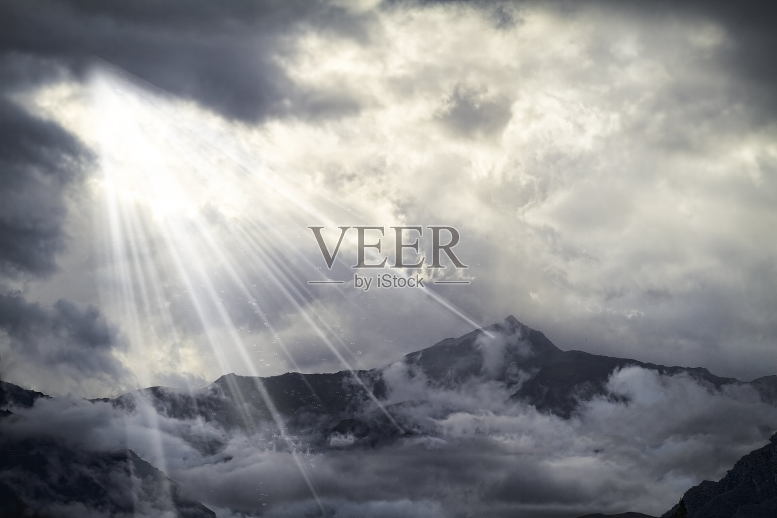 阳光透过阴云洒落，照亮了被薄雾和云层笼罩的山脉景观，传达出宁静而富有诗意的自然场景。照片摄影图片