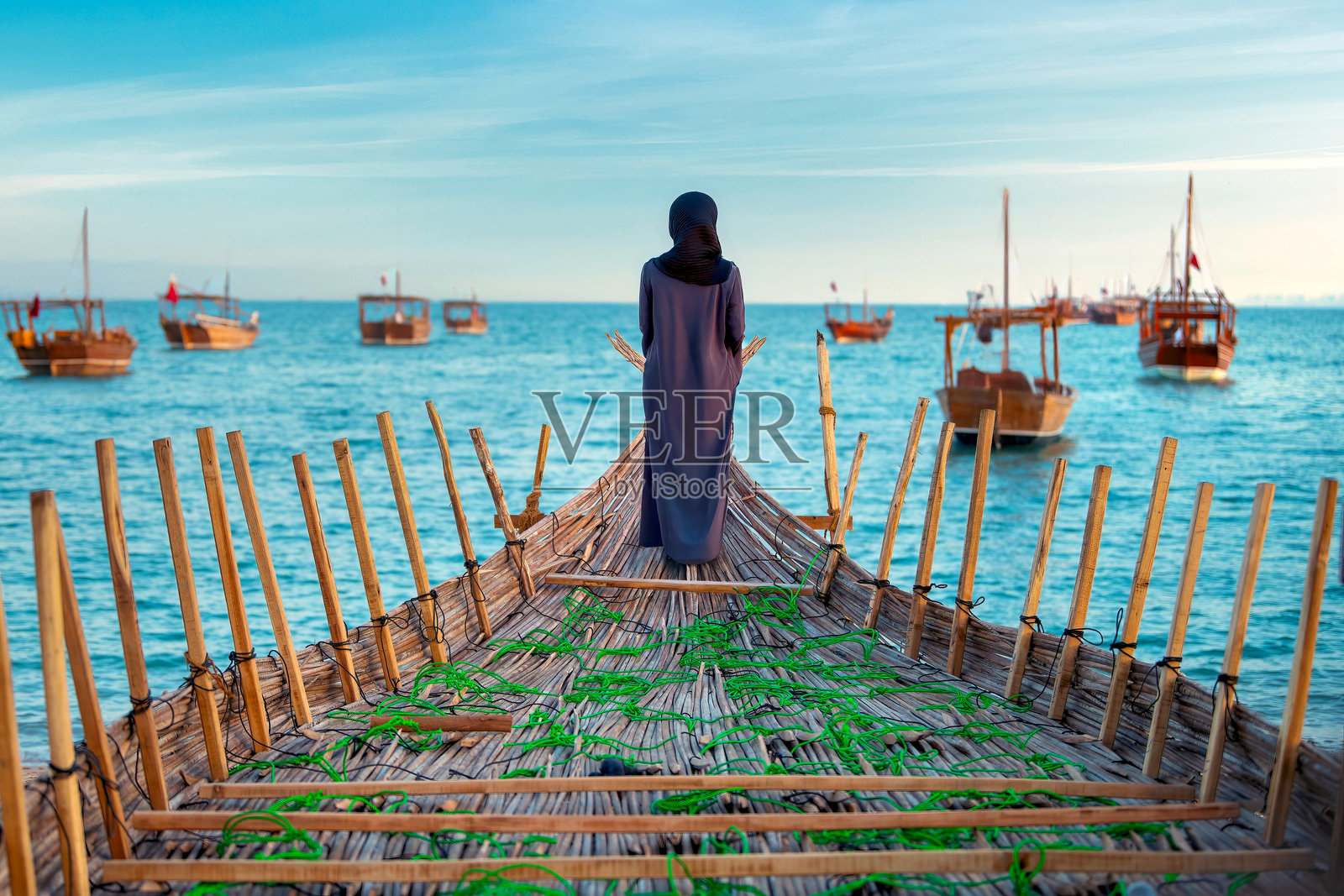 身穿阿巴亚的女性站在传统木制渔船的船头。照片摄影图片