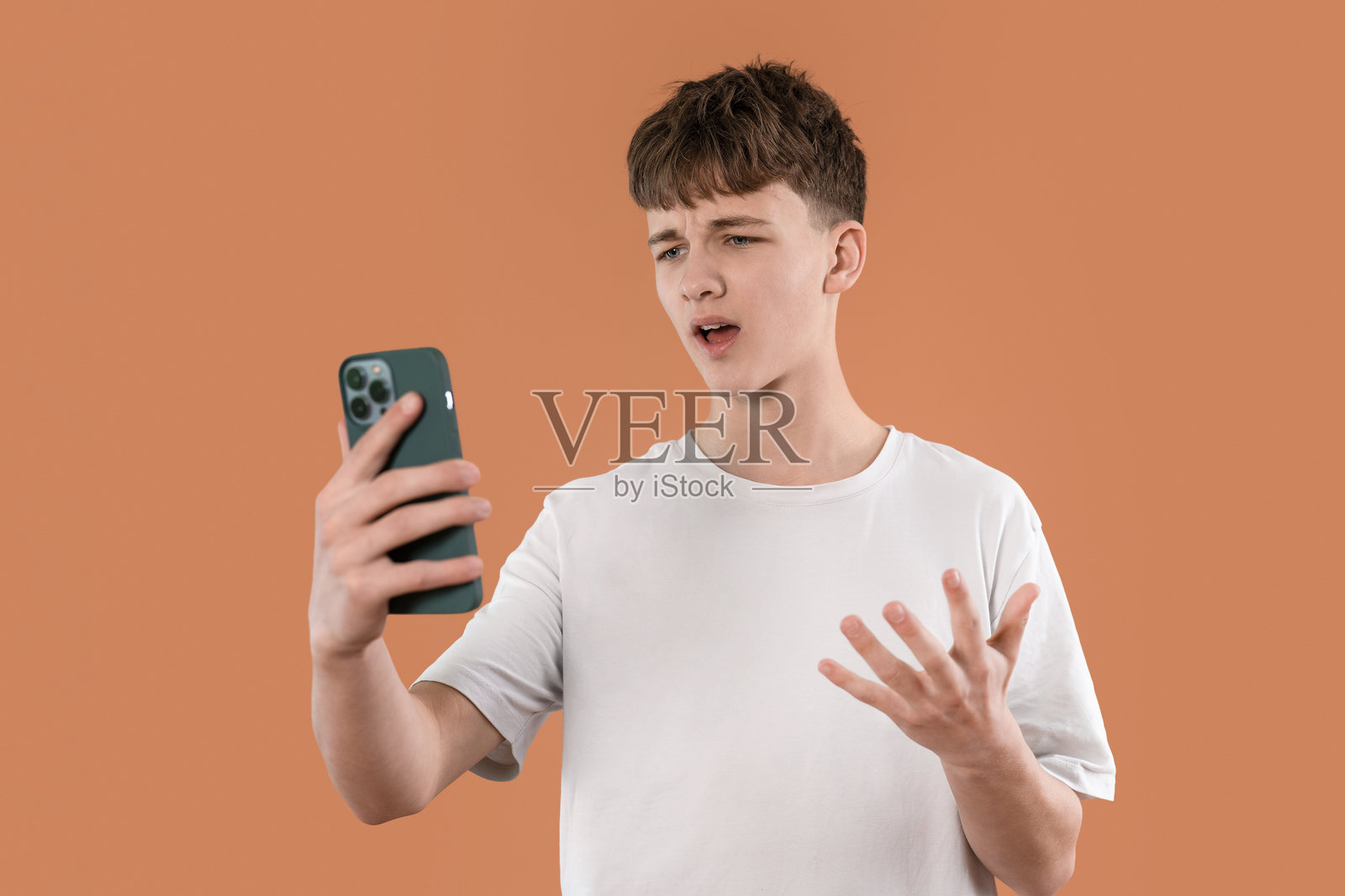 青少年在日间休闲环境中对着橙色背景的智能手机表达沮丧情绪照片摄影图片