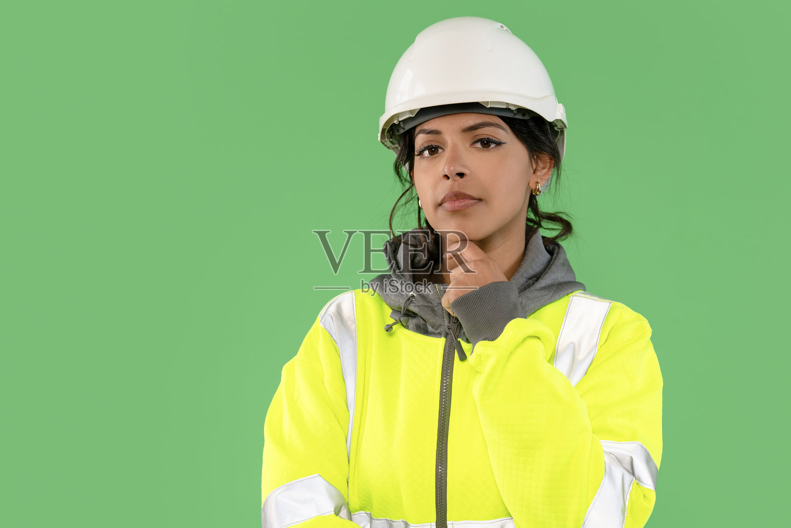 穿着安全装备的建筑工人在明亮的绿色背景前深思熟虑，思考着办公室环境中的一个项目。照片摄影图片