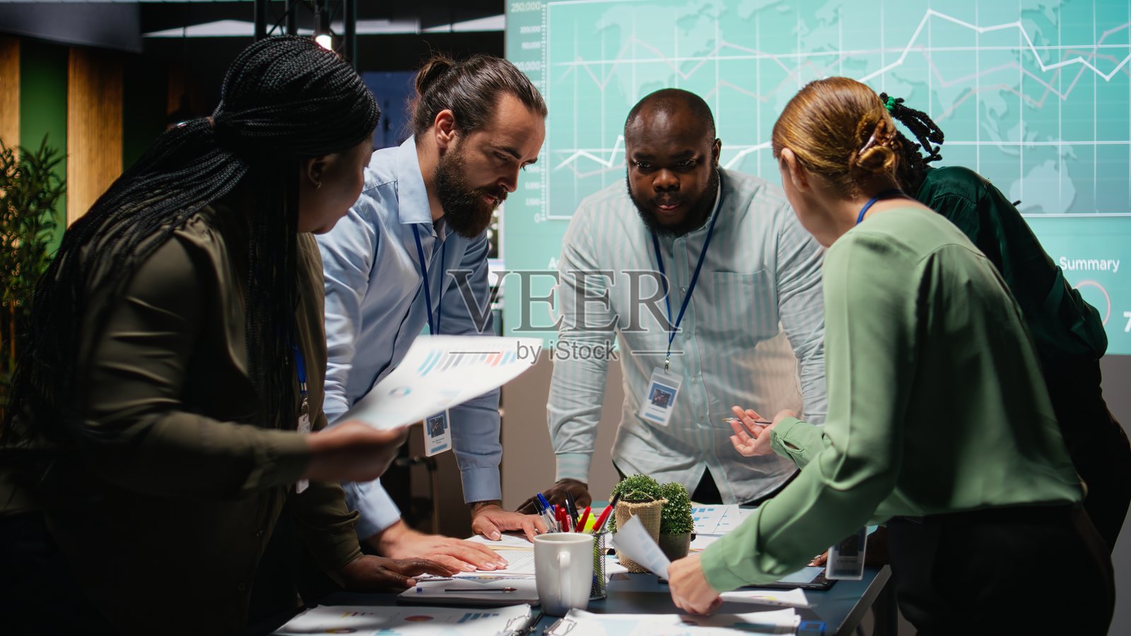 多民族团队在夜间交换文件并审查预测图表照片摄影图片