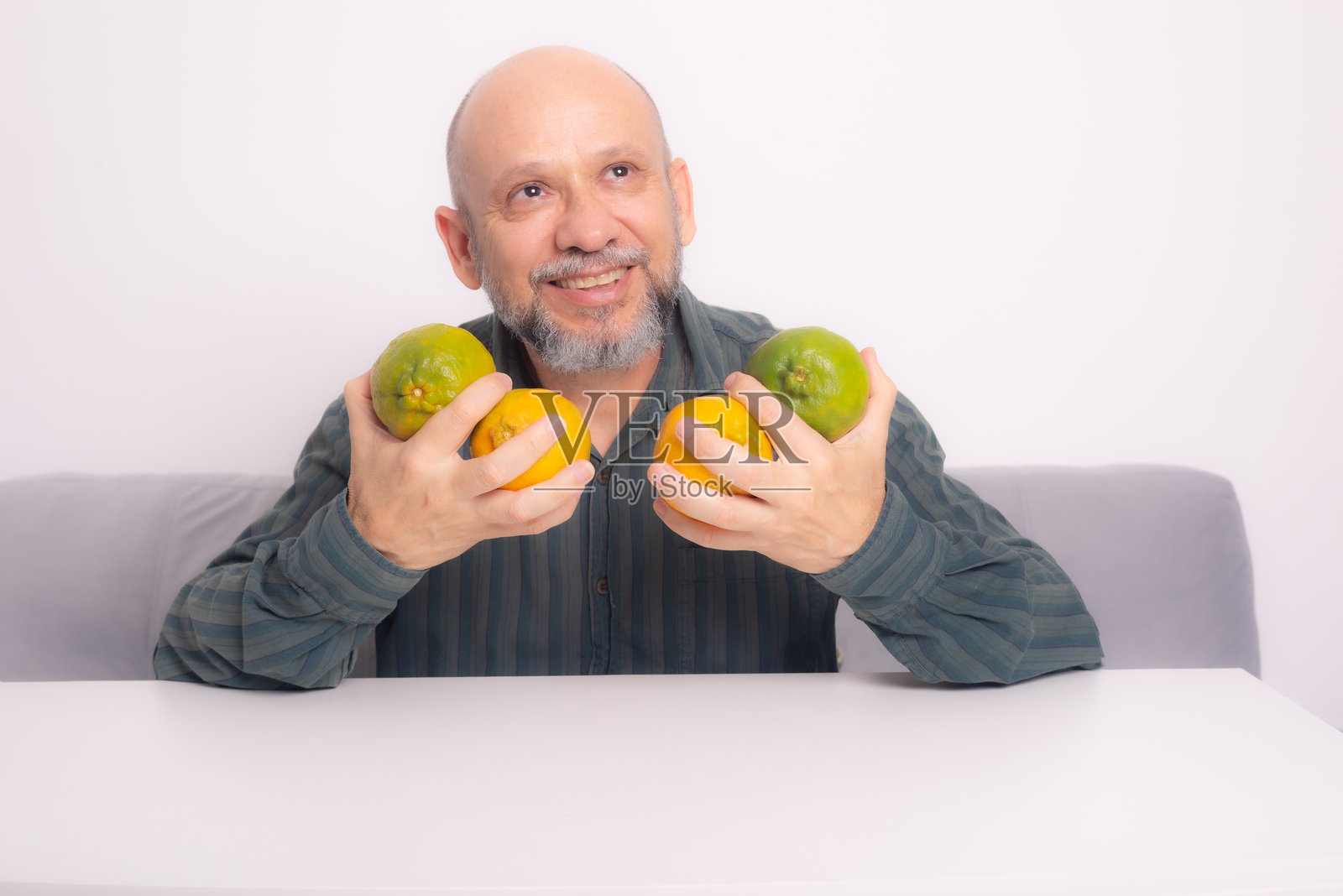 微笑的光头男子，留着胡子，穿着绿色衬衫，手中拿着四个橘子。照片摄影图片