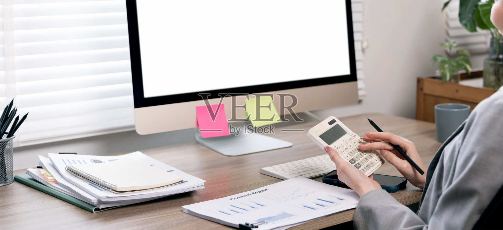 一位女商人在一张桌子上使用计算器，桌上有一台屏幕空白的电脑，背景为全景设计。照片摄影图片