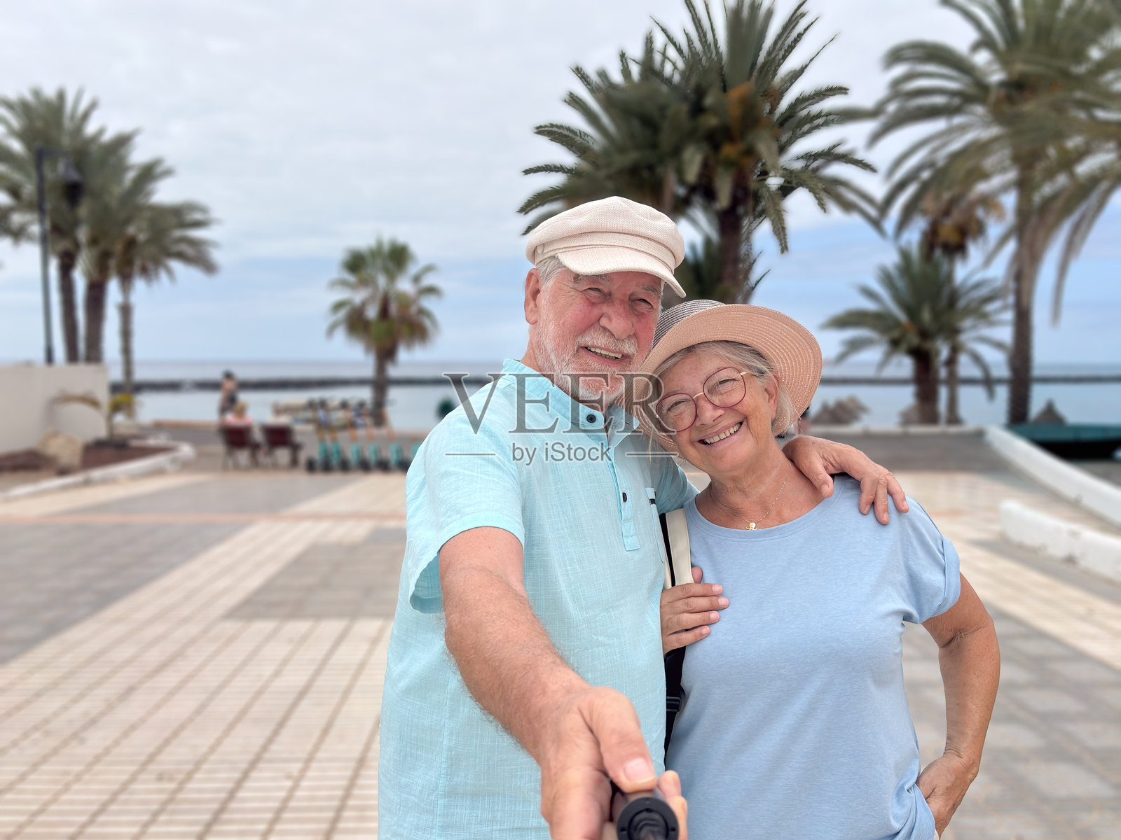 快乐的老年夫妇在热带海滩附近散步时拍摄愉快的自拍照。男士和女士对着镜头温暖地微笑，享受着轻松的假期。照片摄影图片