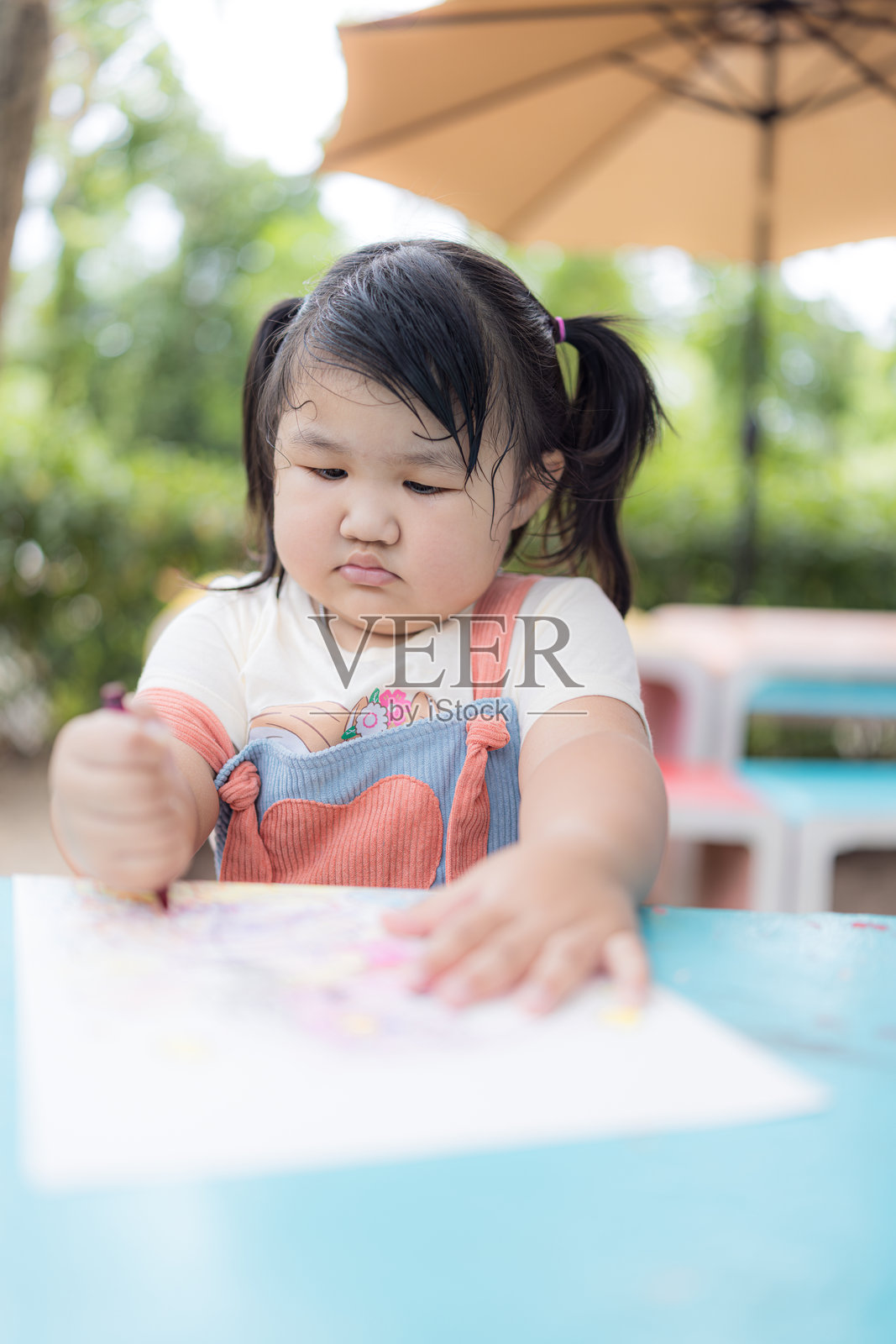 一个可爱的小女孩坐着开心地涂色，亚洲女孩快乐地用蜡笔画画。照片摄影图片