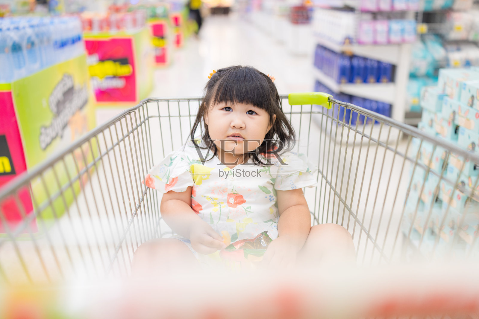 一个可爱、无聊的小女孩坐在购物车上，正在商场里等她的妈妈。照片摄影图片