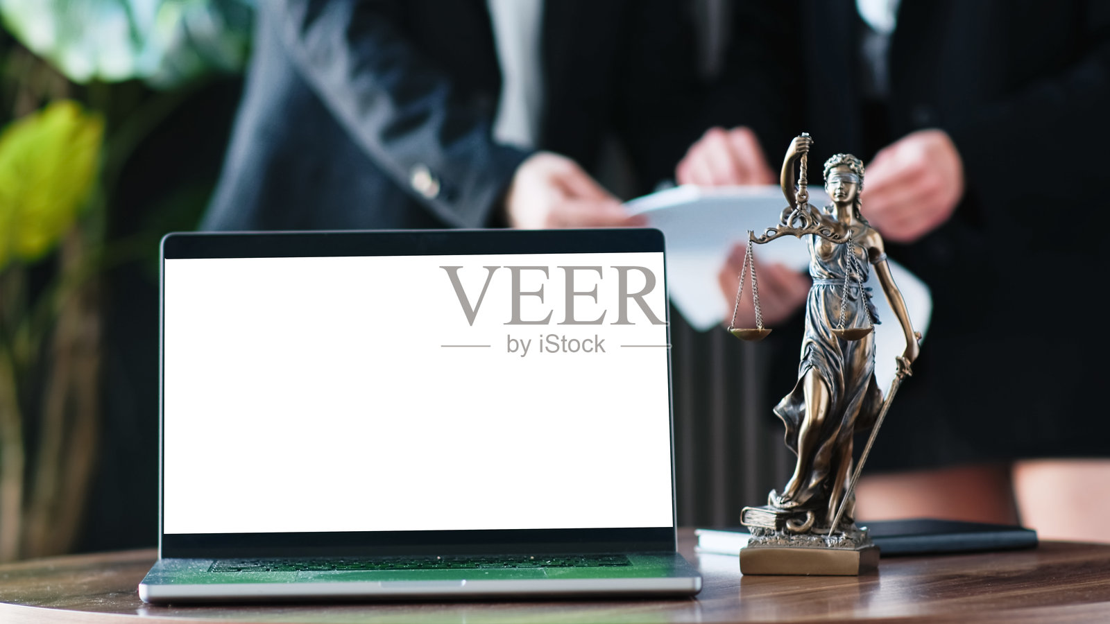 正义女神雕像位于现代办公室中一台空白屏幕的笔记本电脑旁。照片摄影图片