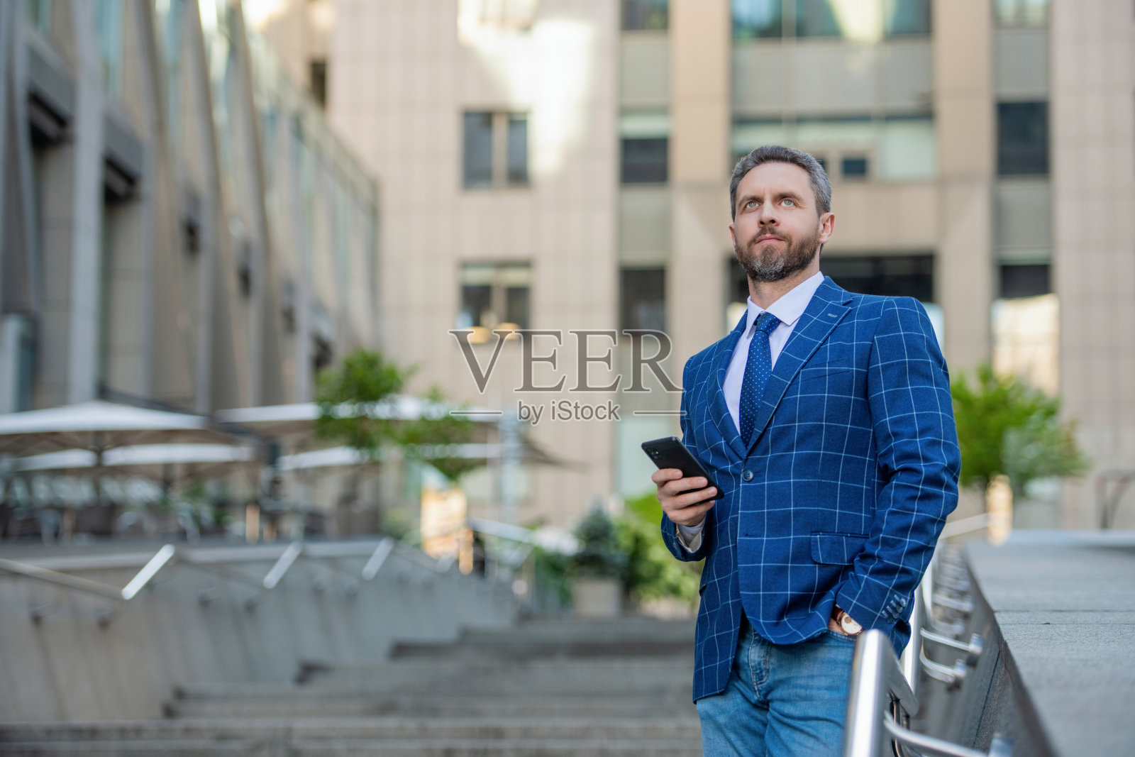 商人在城市中使用手机。商人与手机通话。商人在办公室前面。社交网络。西班牙裔商人在办公大楼内使用手机。留白空间。照片摄影图片