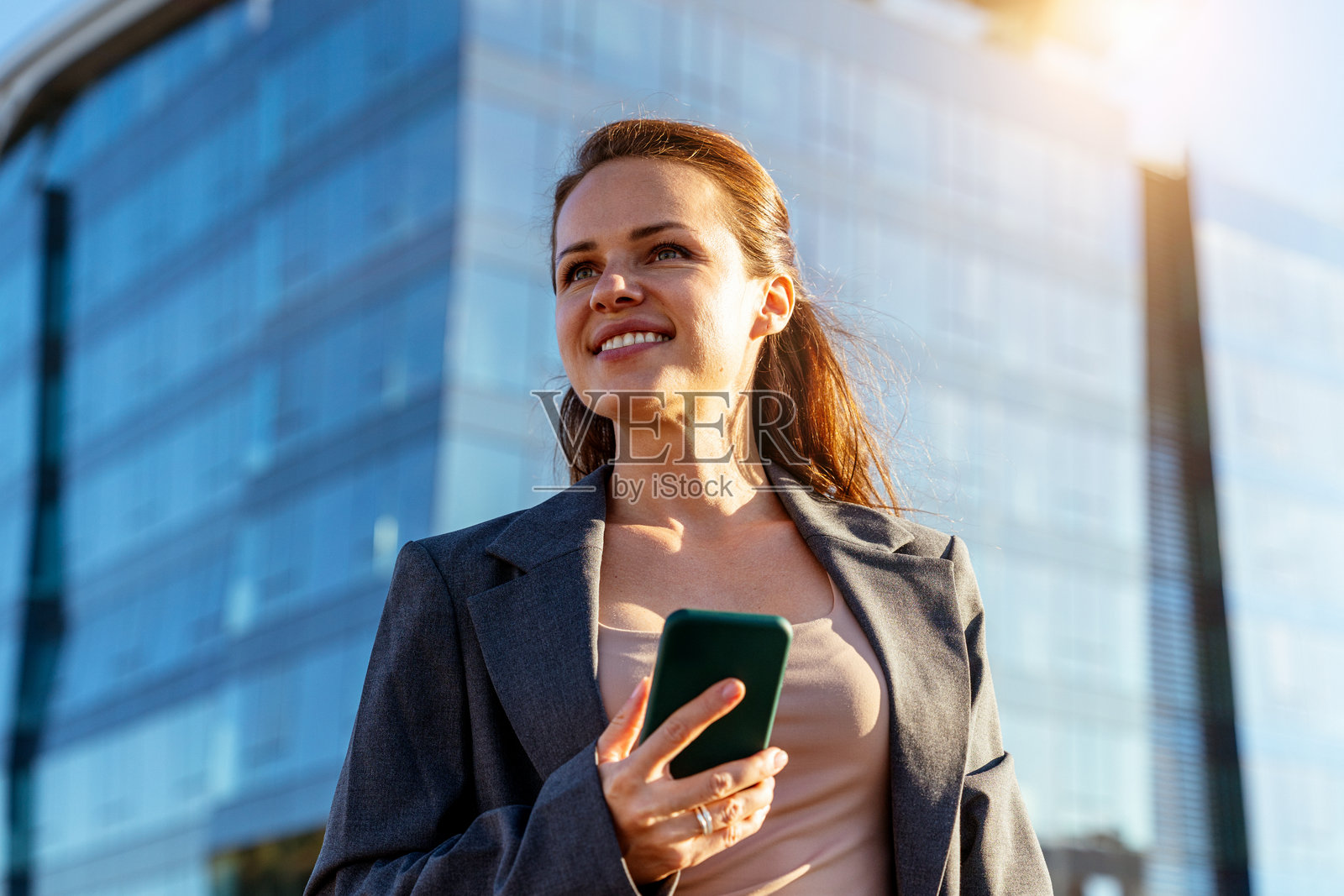 成功的现代女性高管在办公楼前使用智能手机。照片摄影图片