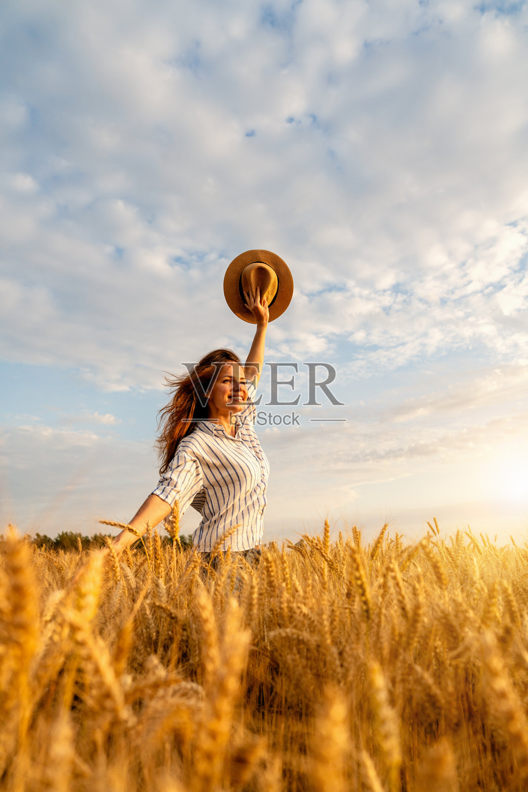 自由奔放的女性在金色麦田中举着草帽，享受宁静的乡村生活照片摄影图片