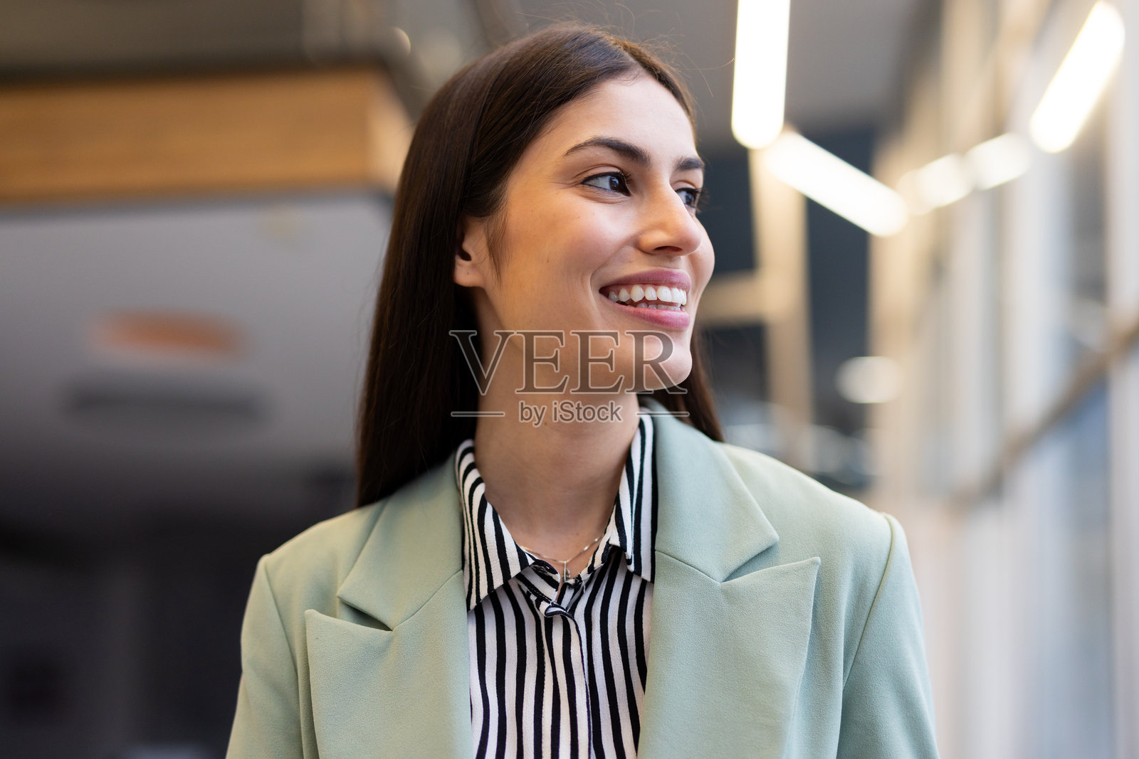 自信的女商人微笑着，转头靠近明亮的办公室走廊窗户。照片摄影图片
