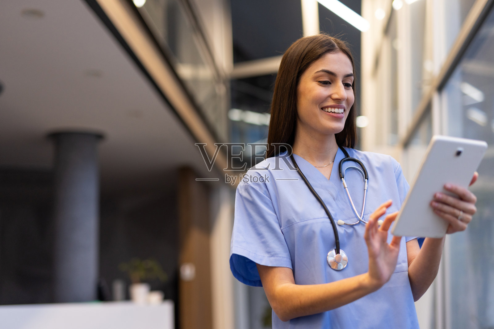 女性医生在医院走廊上自信地走着，微笑着查看平板电脑上的数字健康数据。照片摄影图片