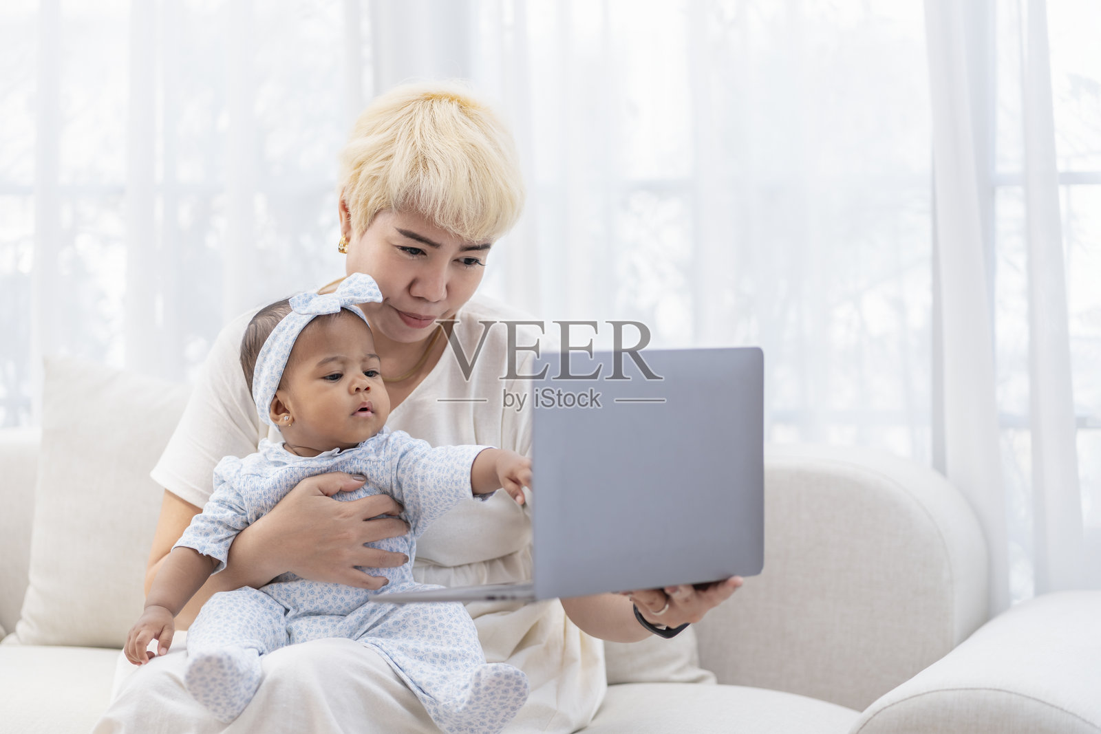 一位亚洲母亲在舒适的客厅里一边照顾宝宝一边使用笔记本电脑照片摄影图片