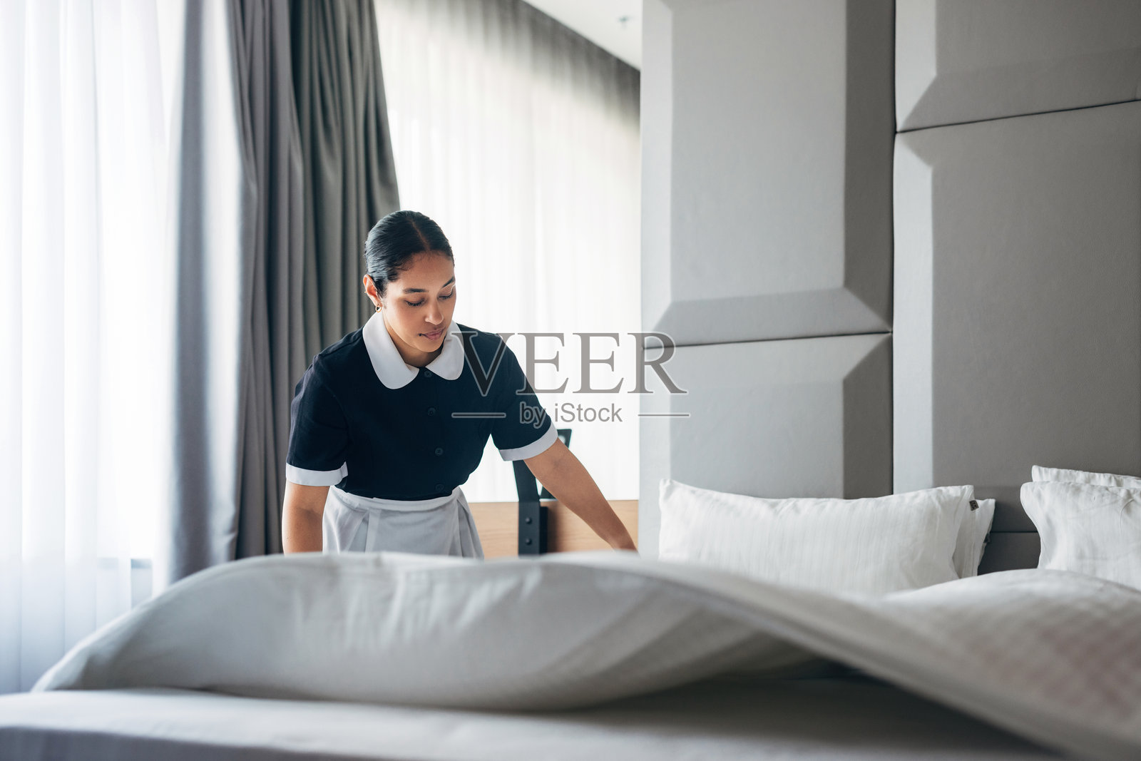 酒店清洁员在现代简约风格的房间内铺床，阳光透入。照片摄影图片