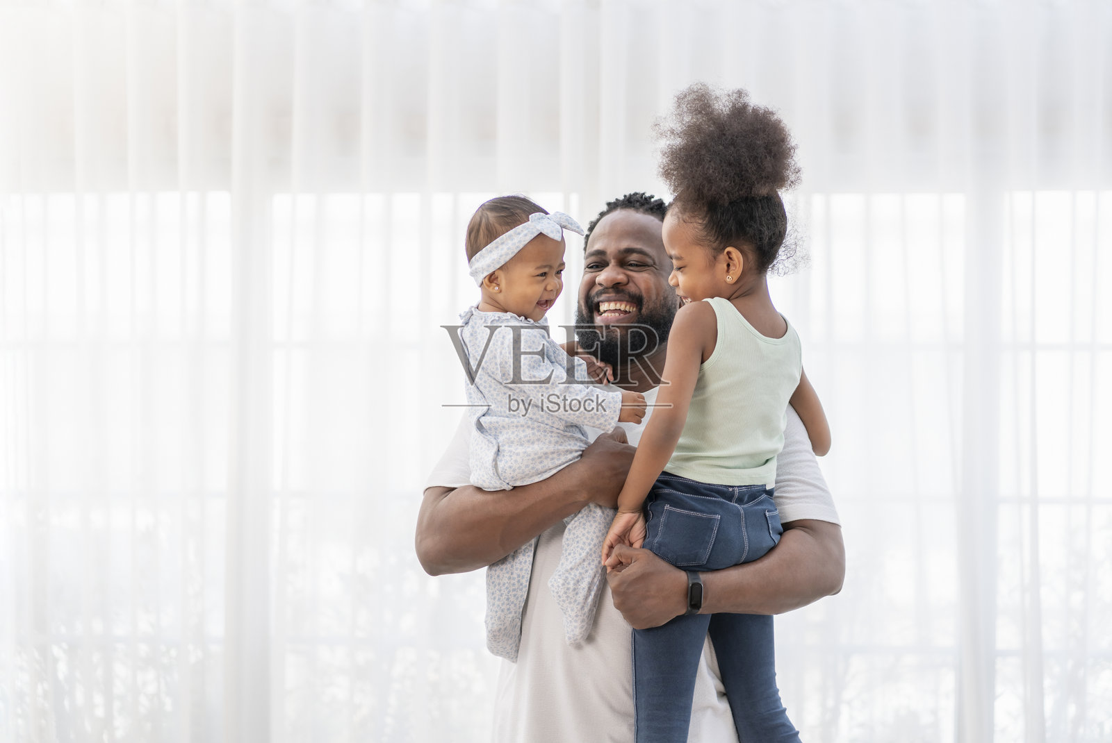 快乐的非洲男性与孩子们在温馨的房间里玩耍，父亲抱着女儿们，大家一起微笑和欢笑。照片摄影图片