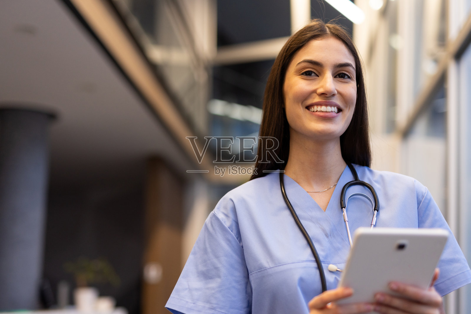 微笑的年轻女医生在现代医院里手持平板电脑，显得自信而友好照片摄影图片