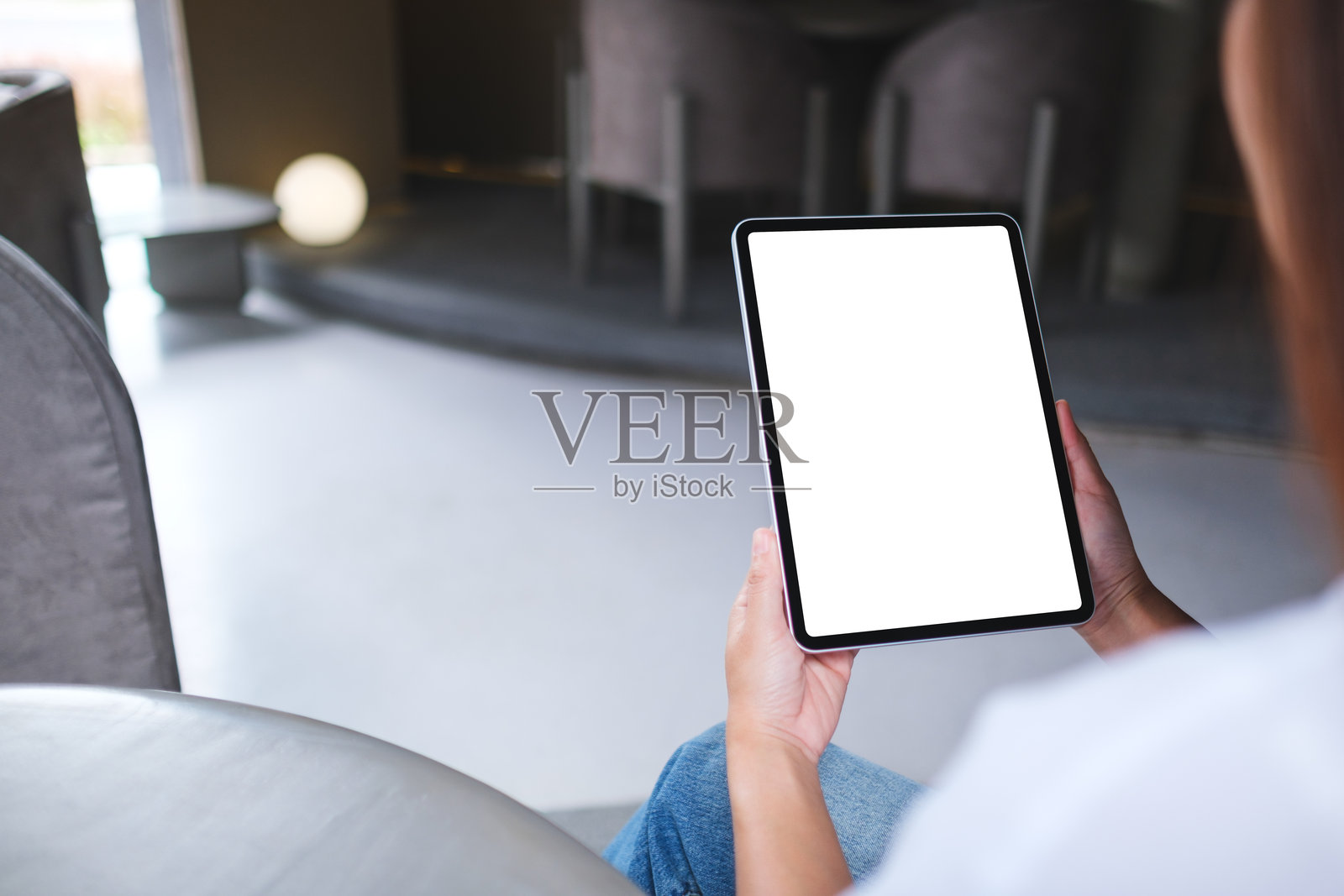 一位女性手持数字平板，屏幕上显示空白的白色桌面。照片摄影图片