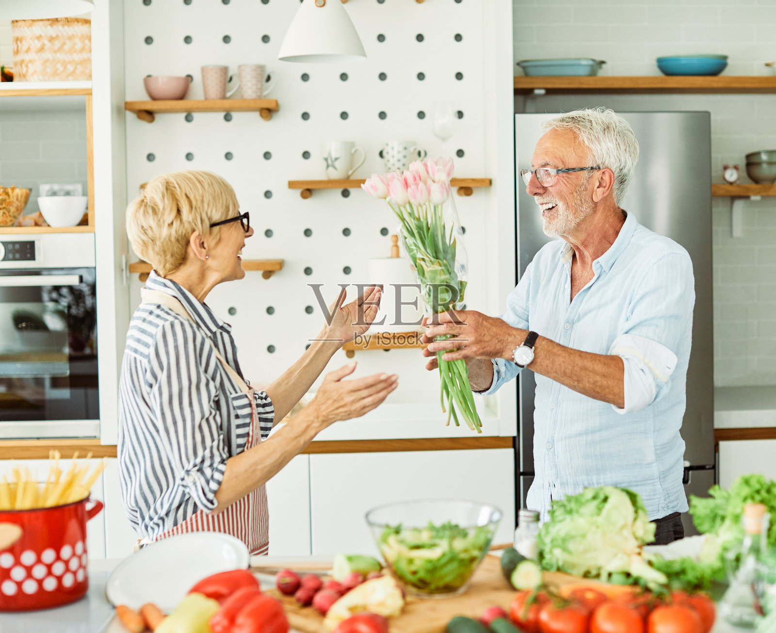 退休快乐的老年夫妇在厨房里，手捧情人节花束照片摄影图片