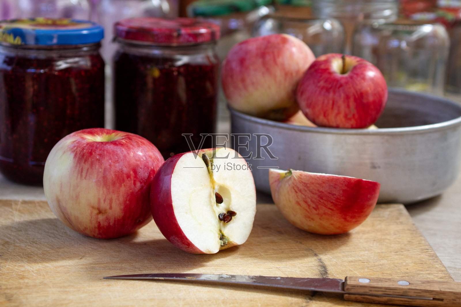 桌子上红色和黄色的苹果，旁边是覆盆子果酱的罐子和背景中的空玻璃罐。照片摄影图片