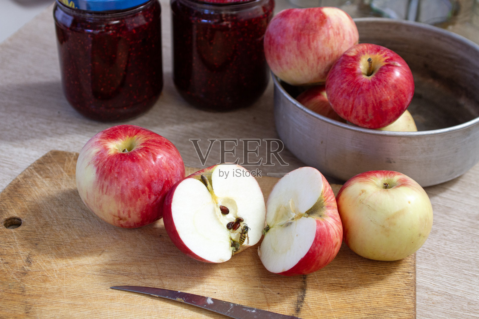 桌子上红色和黄色的苹果，旁边是覆盆子果酱的罐子，背景中有空玻璃罐。照片摄影图片