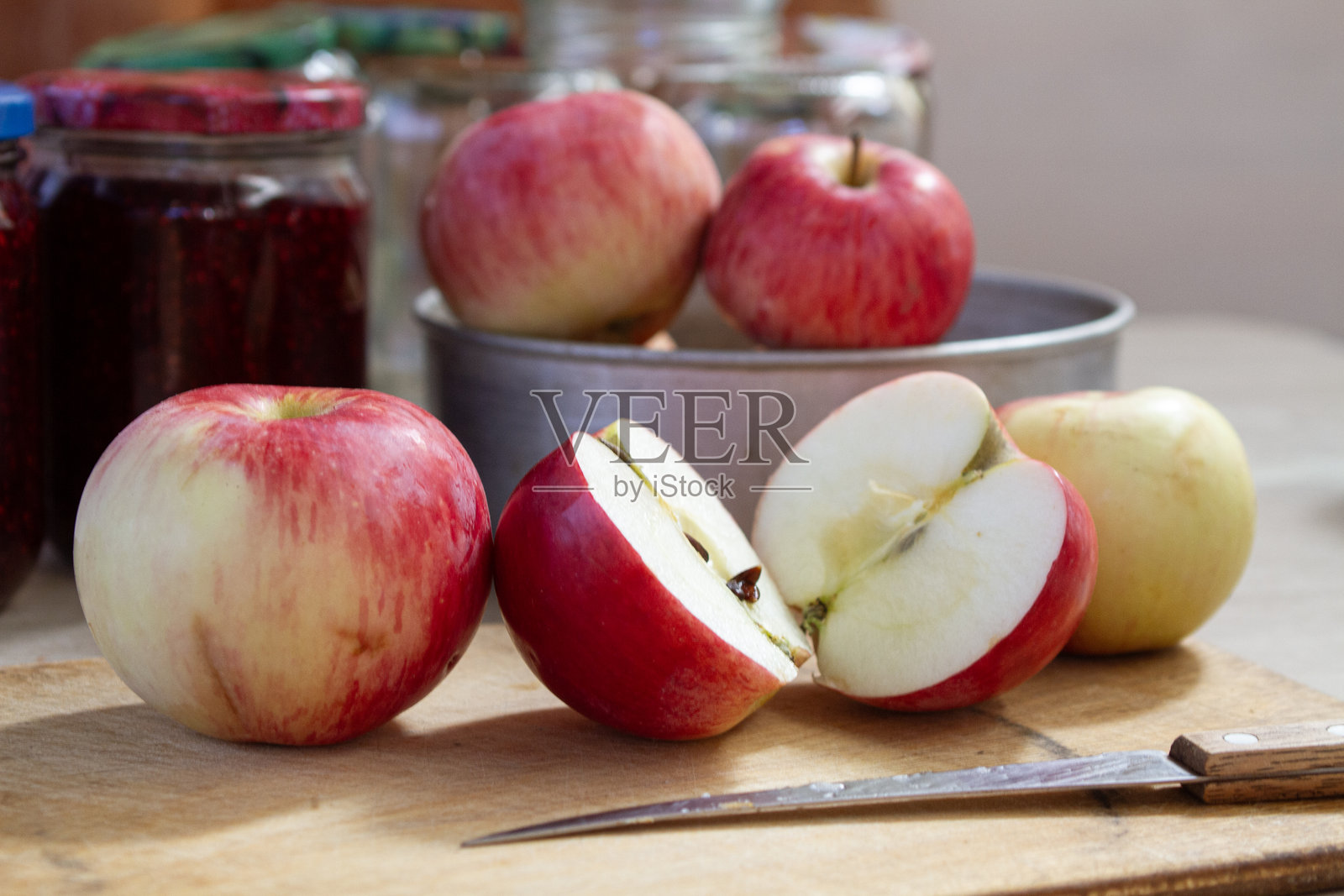 桌子上红色和黄色的苹果，旁边是覆盆子果酱的罐子，背景中有空玻璃罐。照片摄影图片
