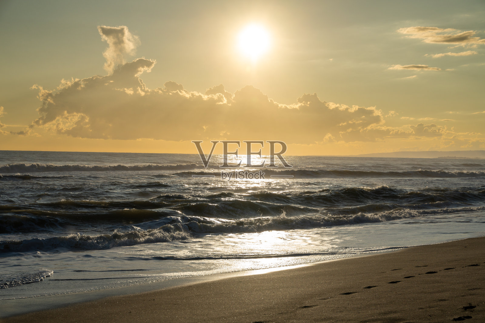 傍晚的阳光和云彩下，海浪在沙滩上拍打。照片摄影图片