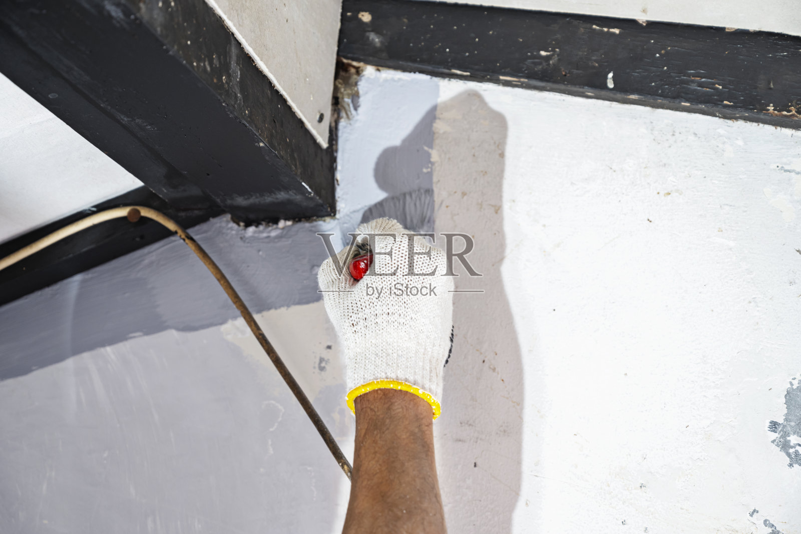 戴手套的建筑工人在进行家庭装修时，使用刷子给墙壁涂漆。家庭装修项目照片摄影图片