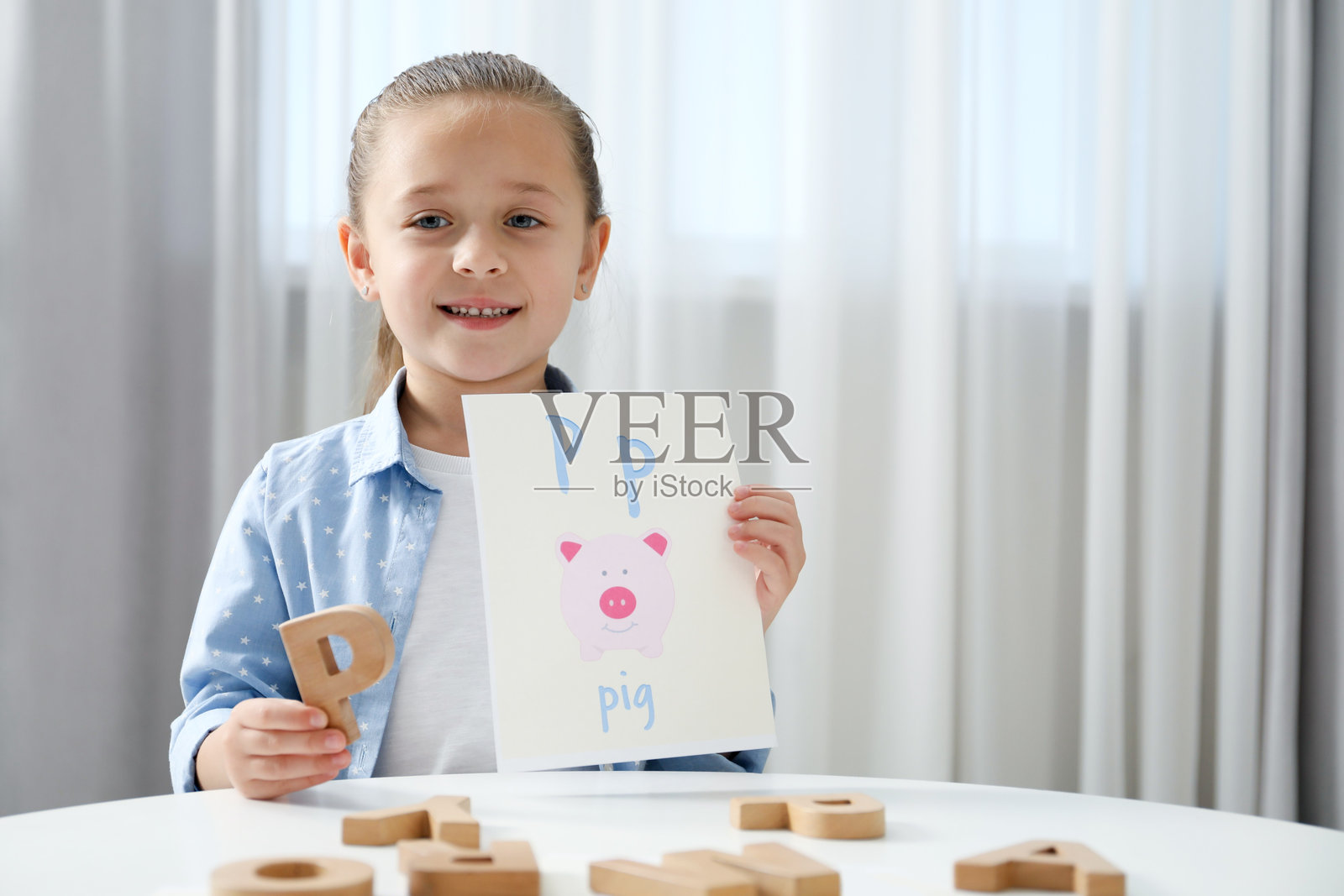 学习字母。小女孩在室内白色桌子上拿着木制字母P和图片，留有文字空间。照片摄影图片
