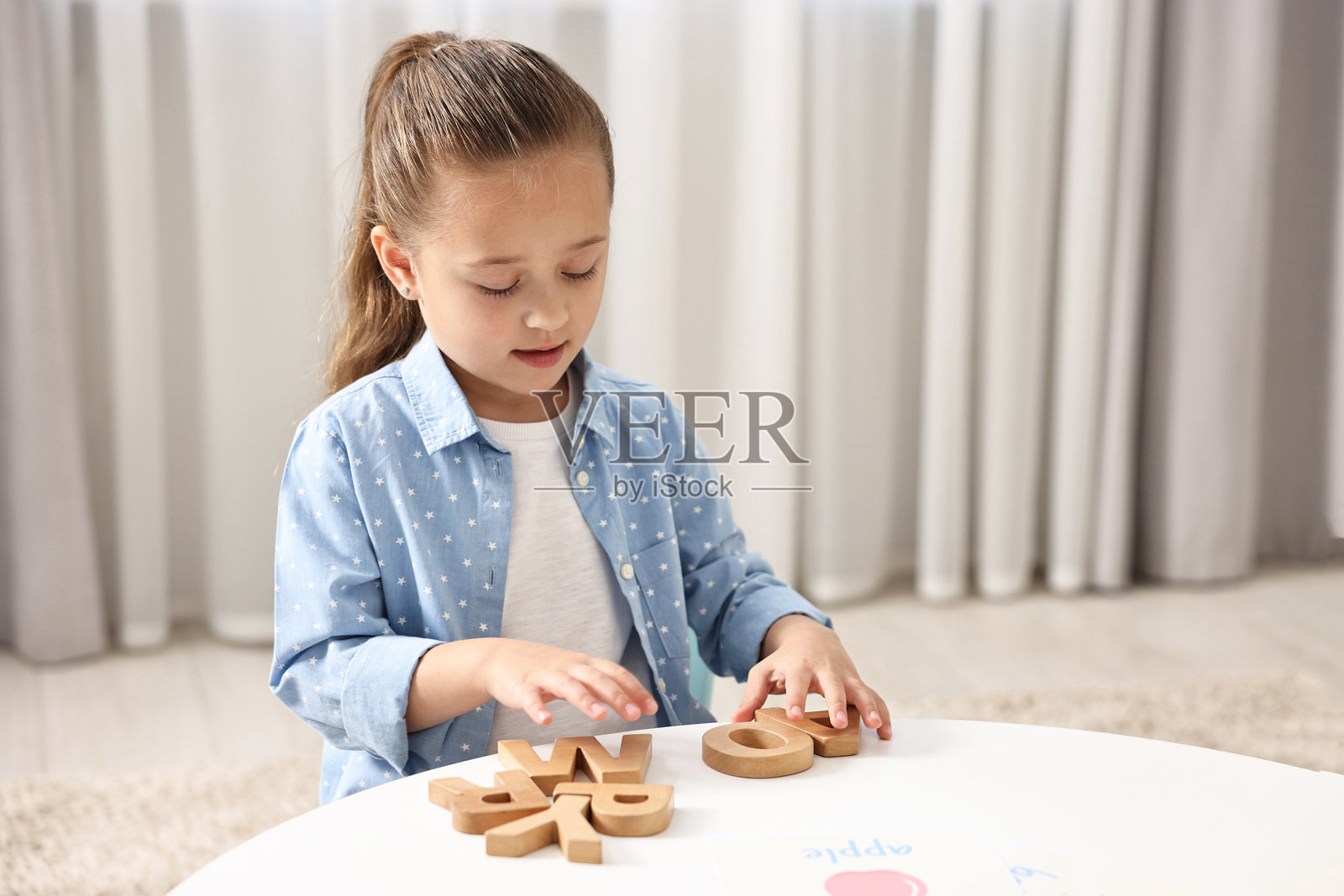 小女孩在室内白色桌子上用木制字母学习字母表，留有文字空间照片摄影图片
