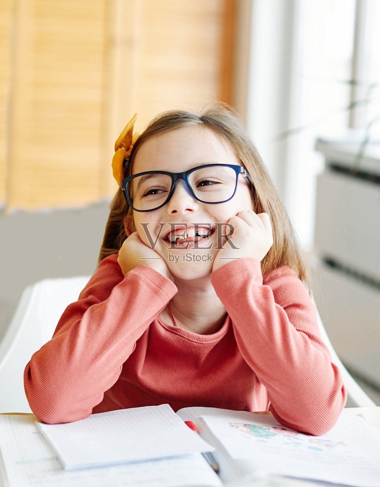 女孩在家学习，专心做作业，坐在书桌前，手里拿着可爱的笔记本，快乐的小学生。照片摄影图片
