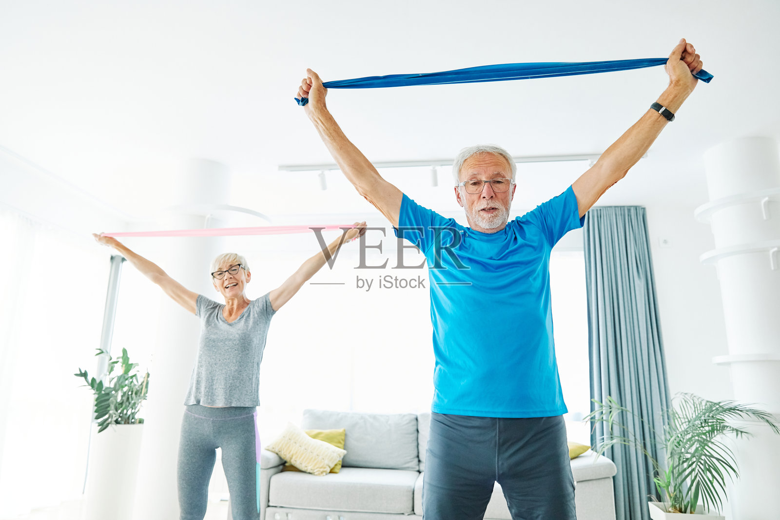 活跃的老年夫妇在家中使用弹性阻力带进行运动训练，增强力量和拉伸，进行普拉提健身。照片摄影图片