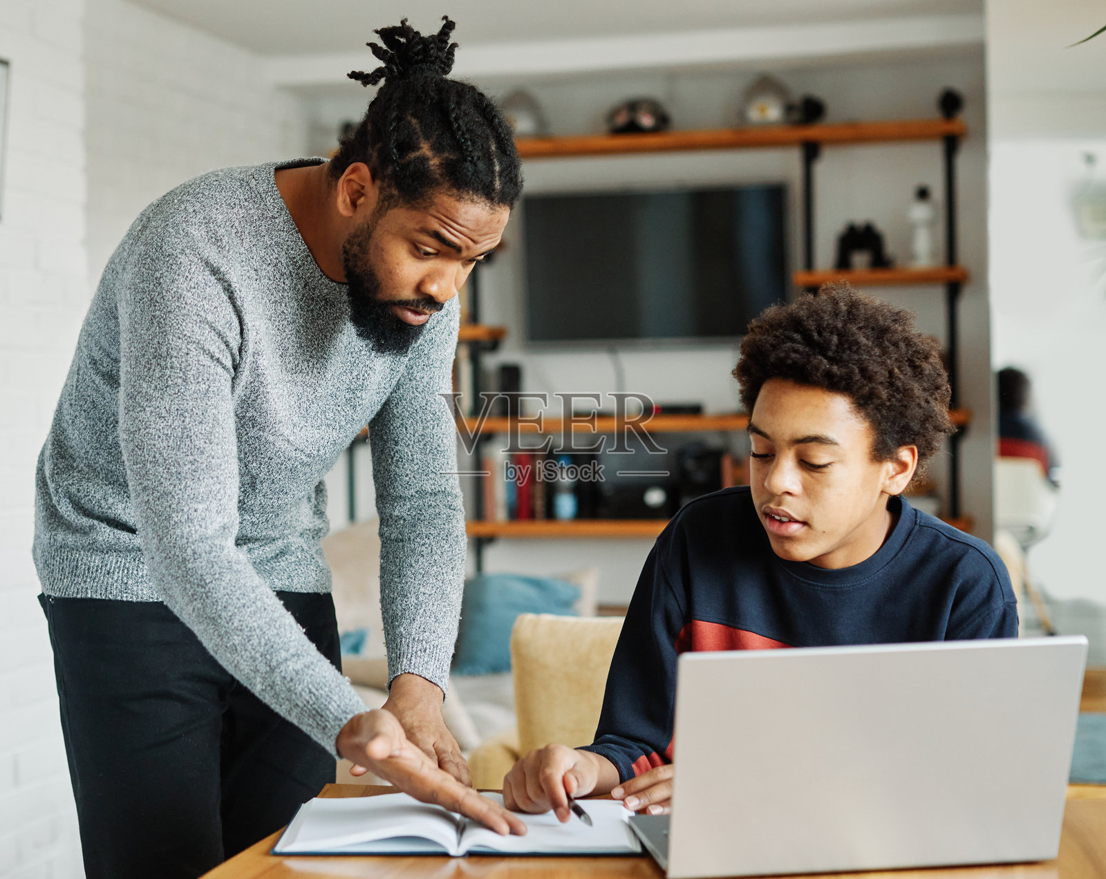 父亲与儿子在家中一起做作业，家庭教育中出现争吵，父亲感到无聊、疲惫、拒绝、恼怒，儿子则分心于笔记本电脑，父亲在教导儿子，两人共同学习。照片摄影图片