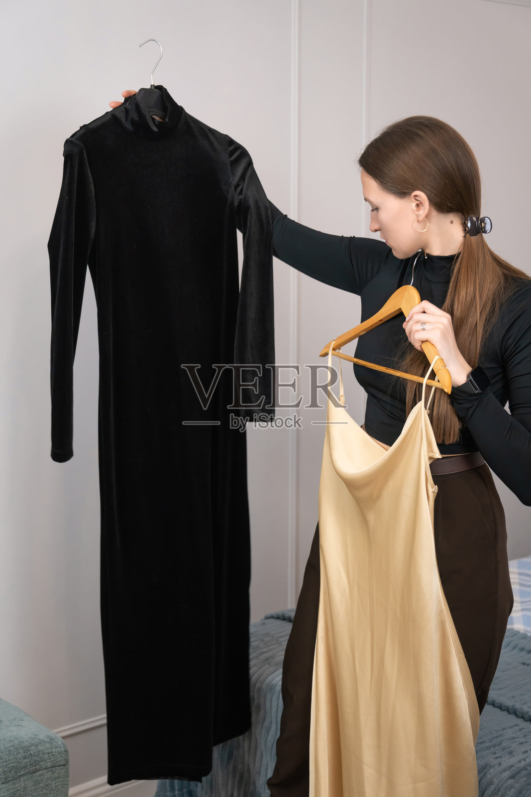 专业时装设计师手持两件衣服在比较，一件黑色天鹅绒裙子和一件金色丝绸裙子，同时决定哪一件更适合她的新系列。竖版照片照片摄影图片