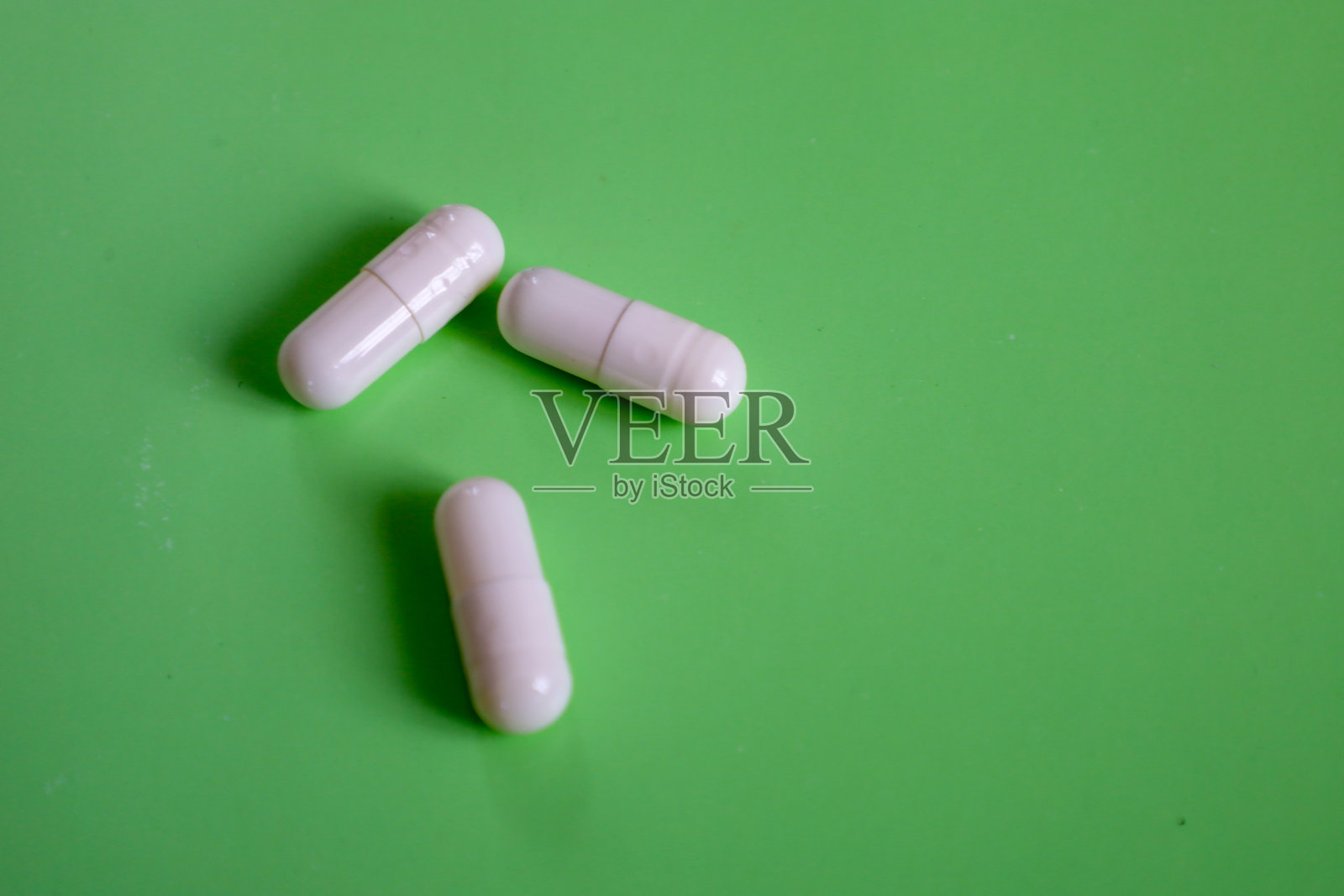 三颗白色胶囊放置在干净的绿色背景上，形成了简单而富有表现力的构图。该图像非常适合用于可视化与健康、治疗和制药行业相关的概念。照片摄影图片