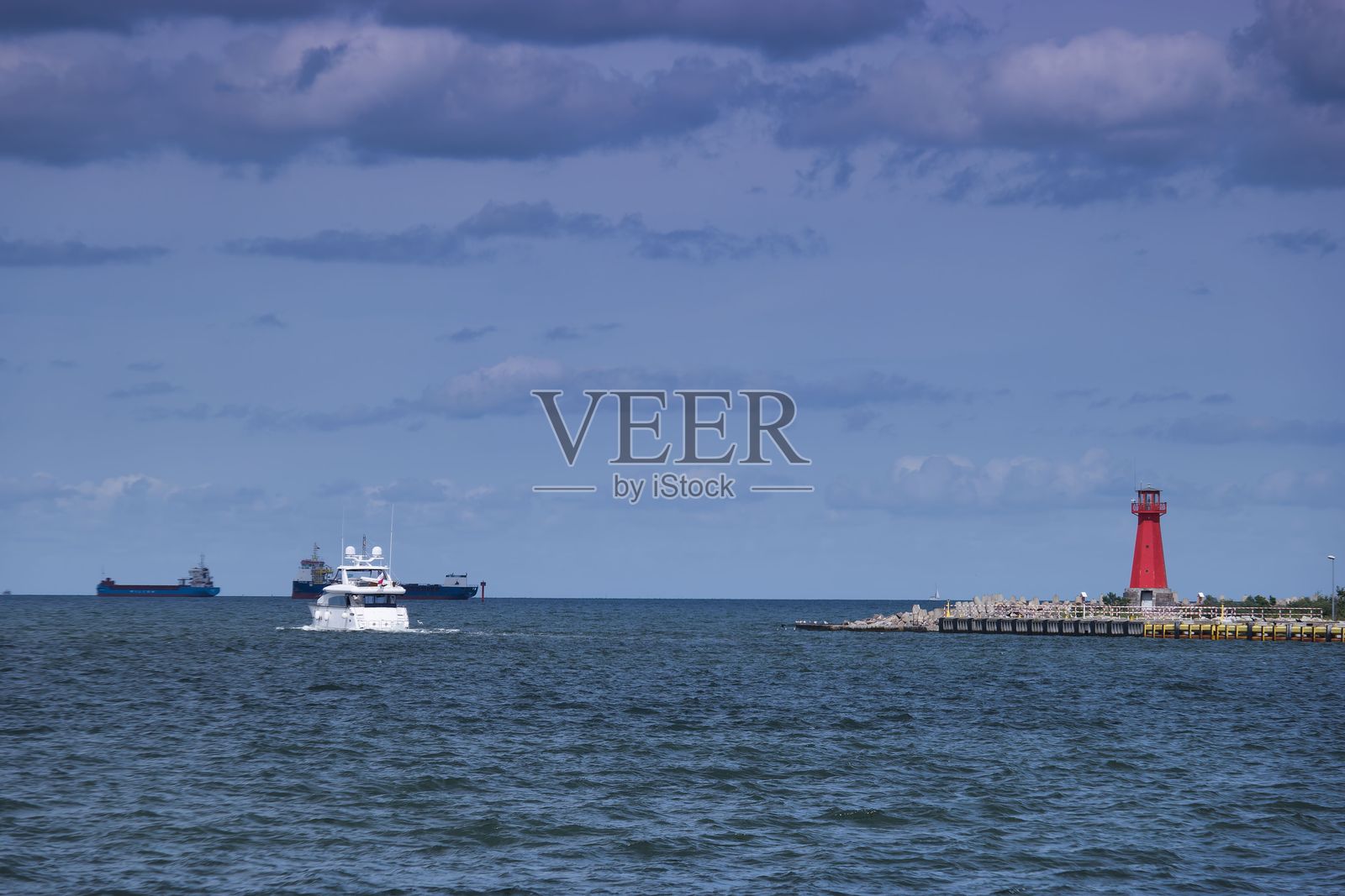 船只在红色灯塔附近航行，平静的水面上有船只，天空多云。照片摄影图片